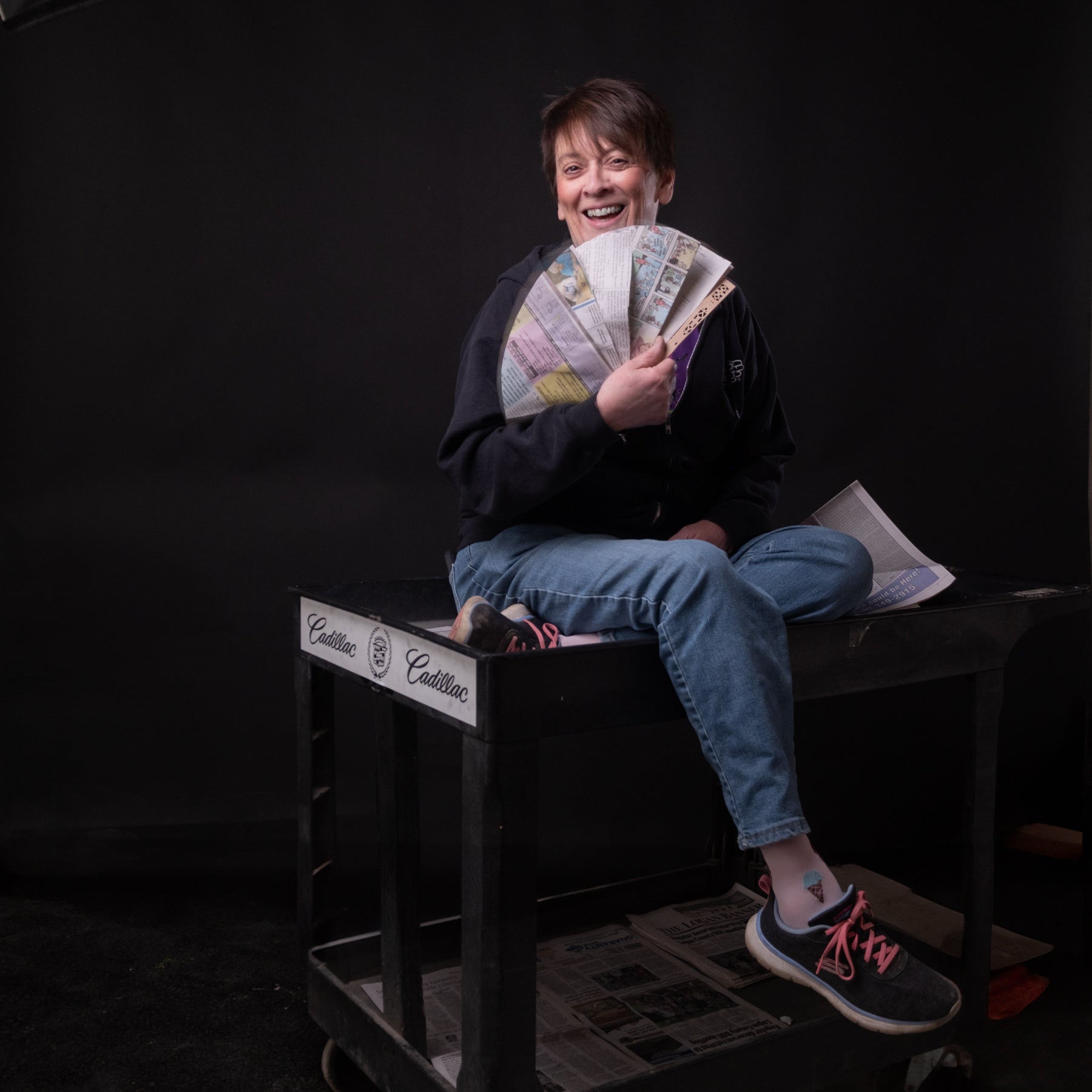 Person sitting on a black crate holding money against a dark background