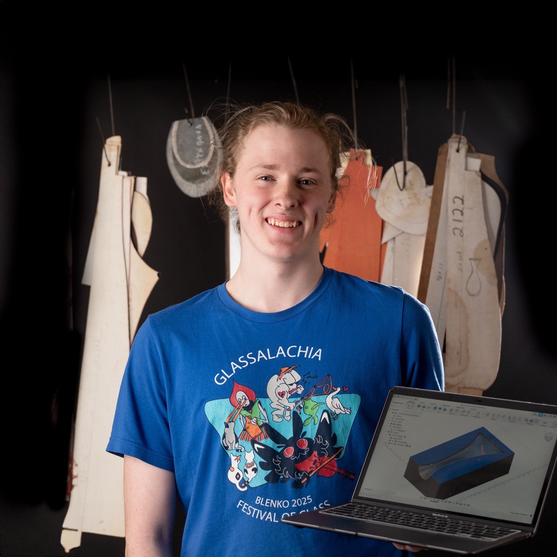 Person holding a laptop with a colorful design in front of a black background with hanging fabrics.