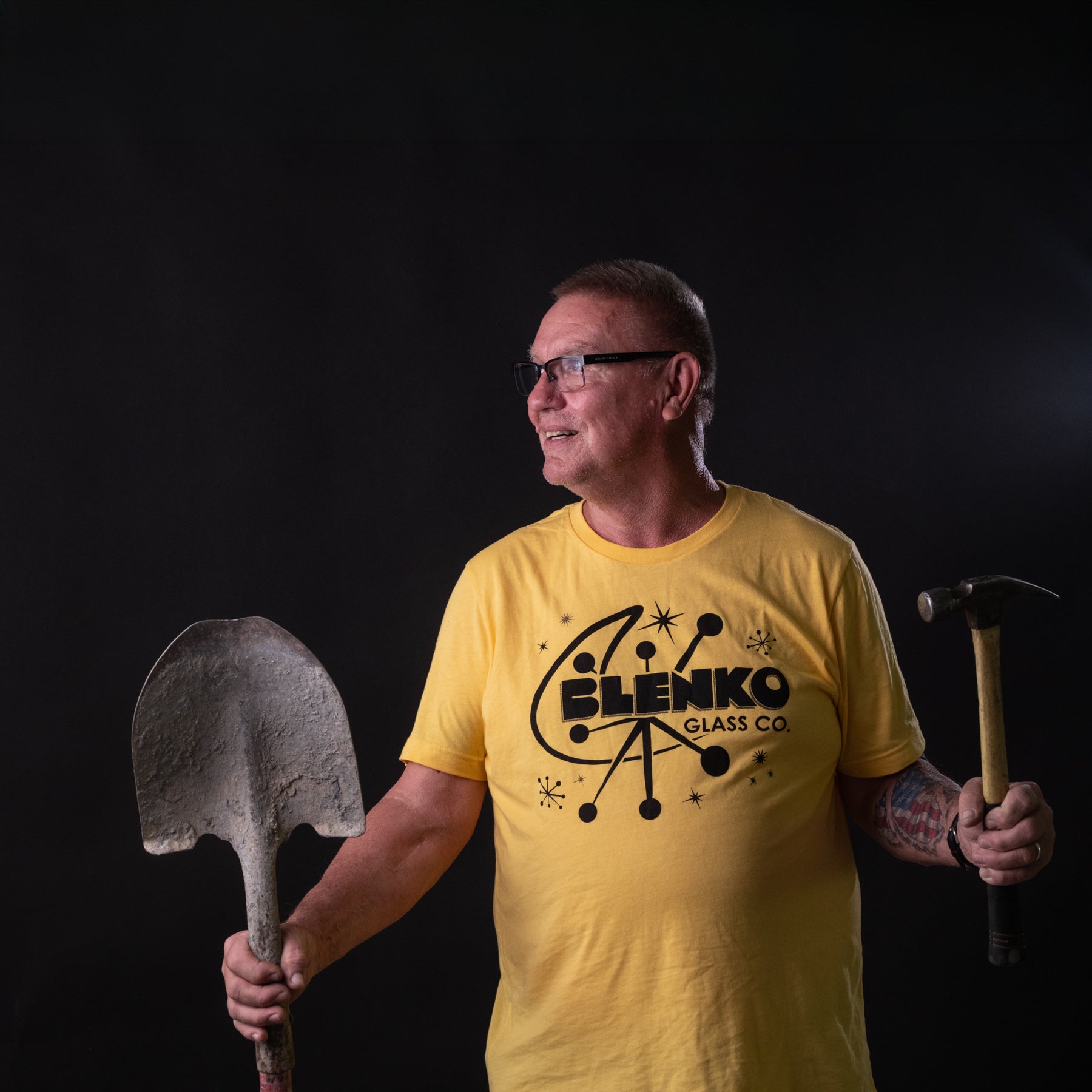 Guy in a yellow shirt holding a shovel and hammer.