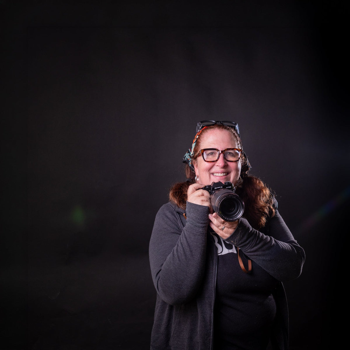 Lady with a camera standing in front of a black background.