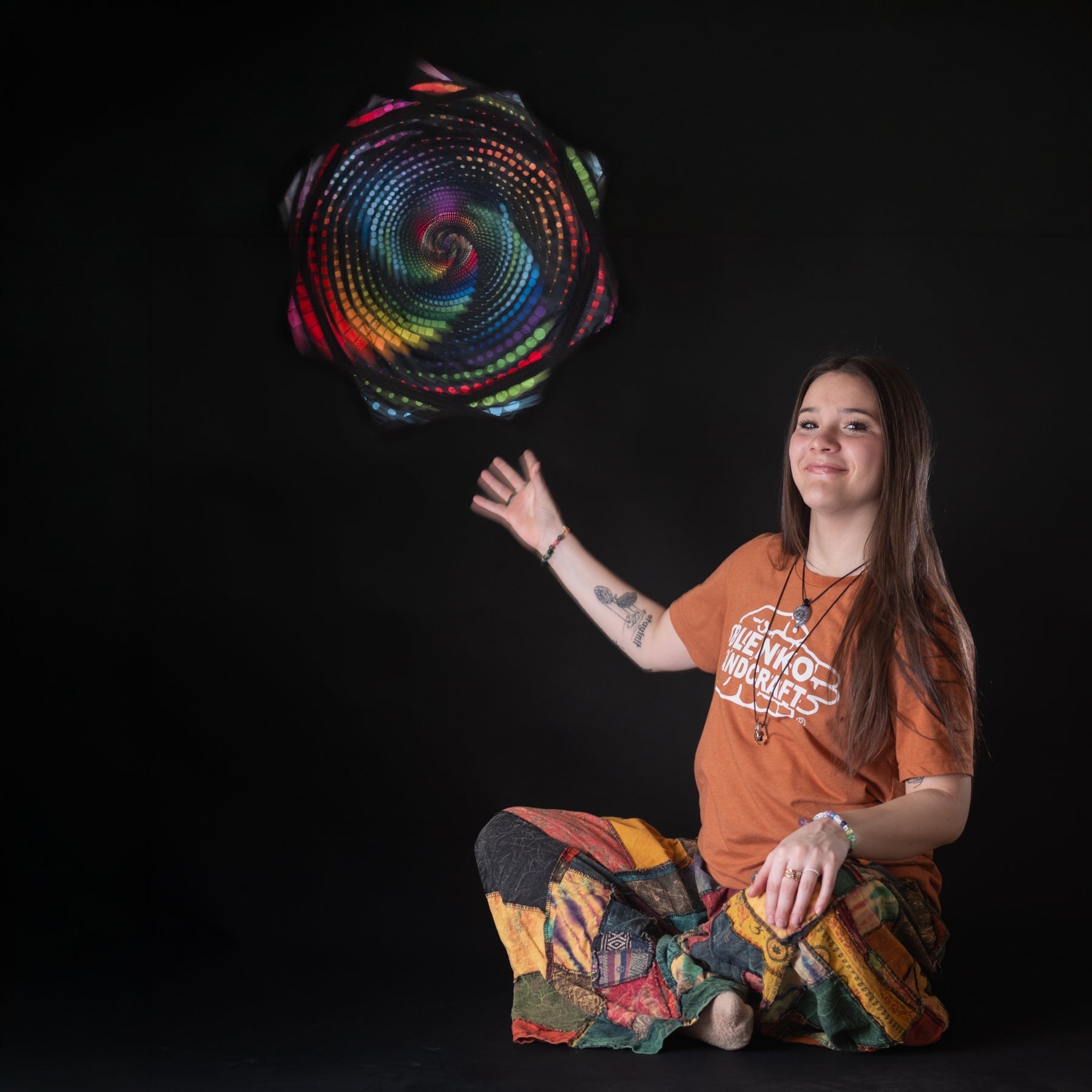 Person sitting on the ground with a colorful, patterned pillow above them against a black background
