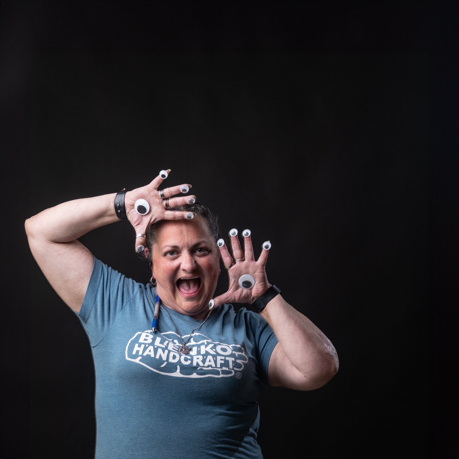 Person wearing gloves with googly eyes and a blue t-shirt with 'Blenko Handcrafts' logo on a black background