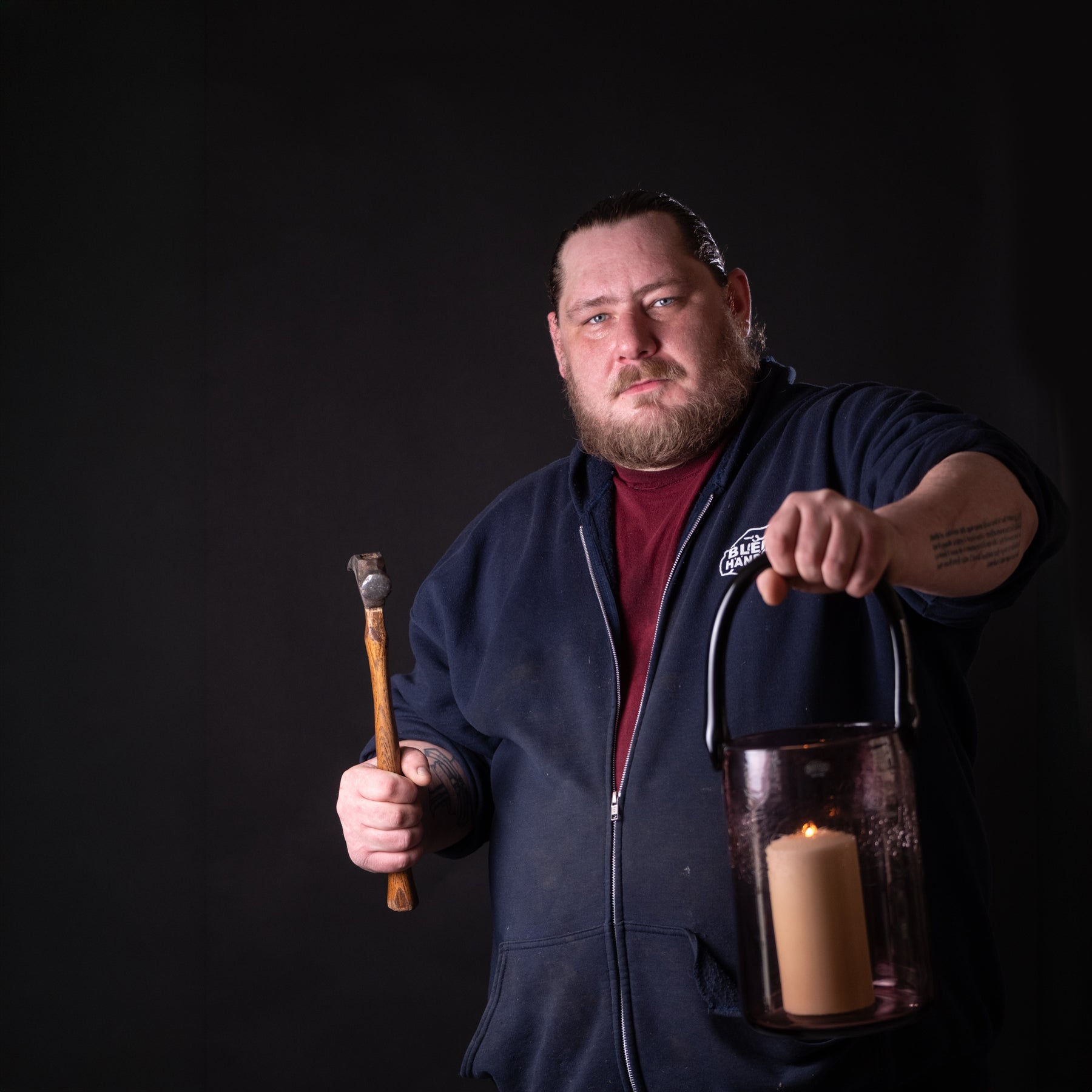Man holding a lantern and a wooden tool against a black background