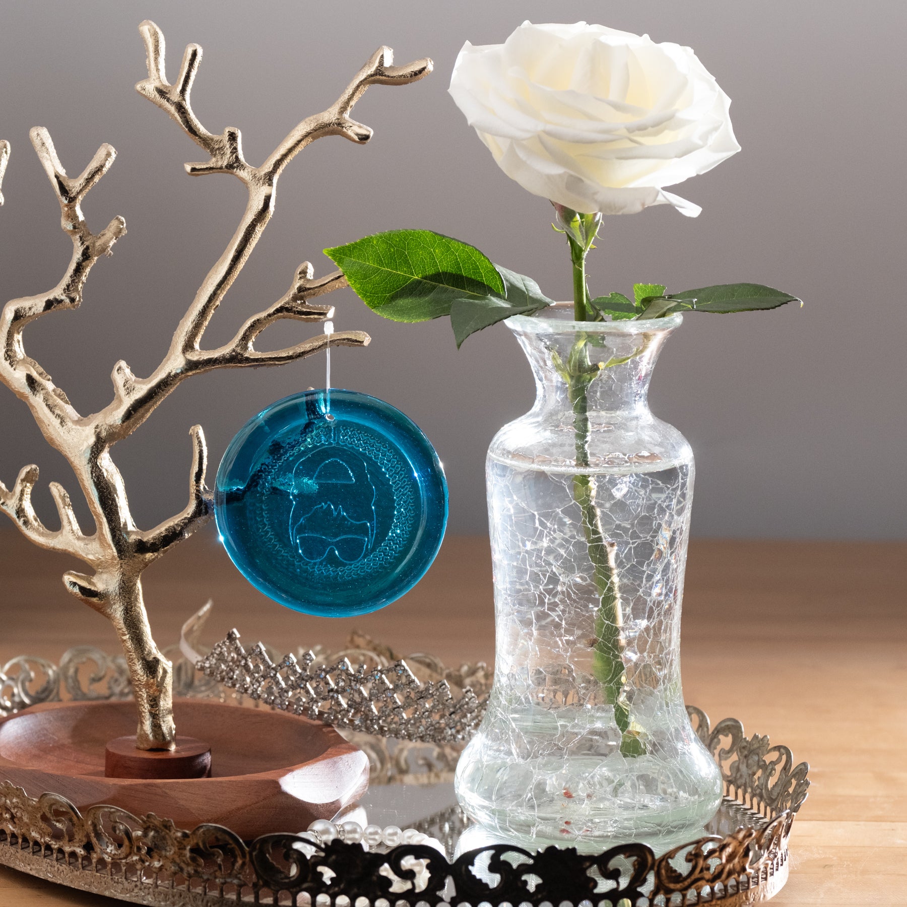 Crystal vase with white rose flower beside a turquoise suncatcher