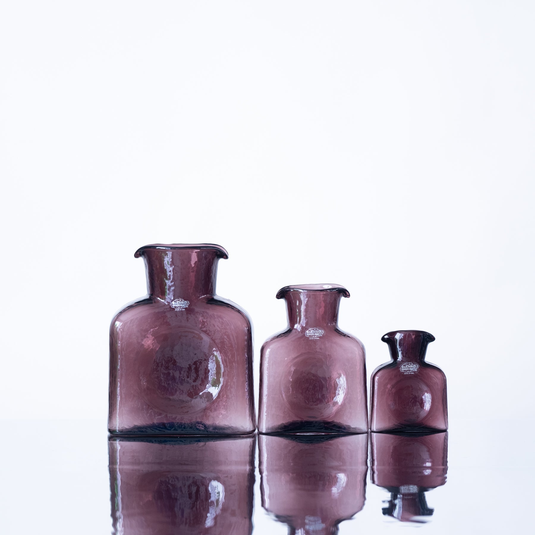 Three pink glass vases of different sizes on a reflective surface with a white background