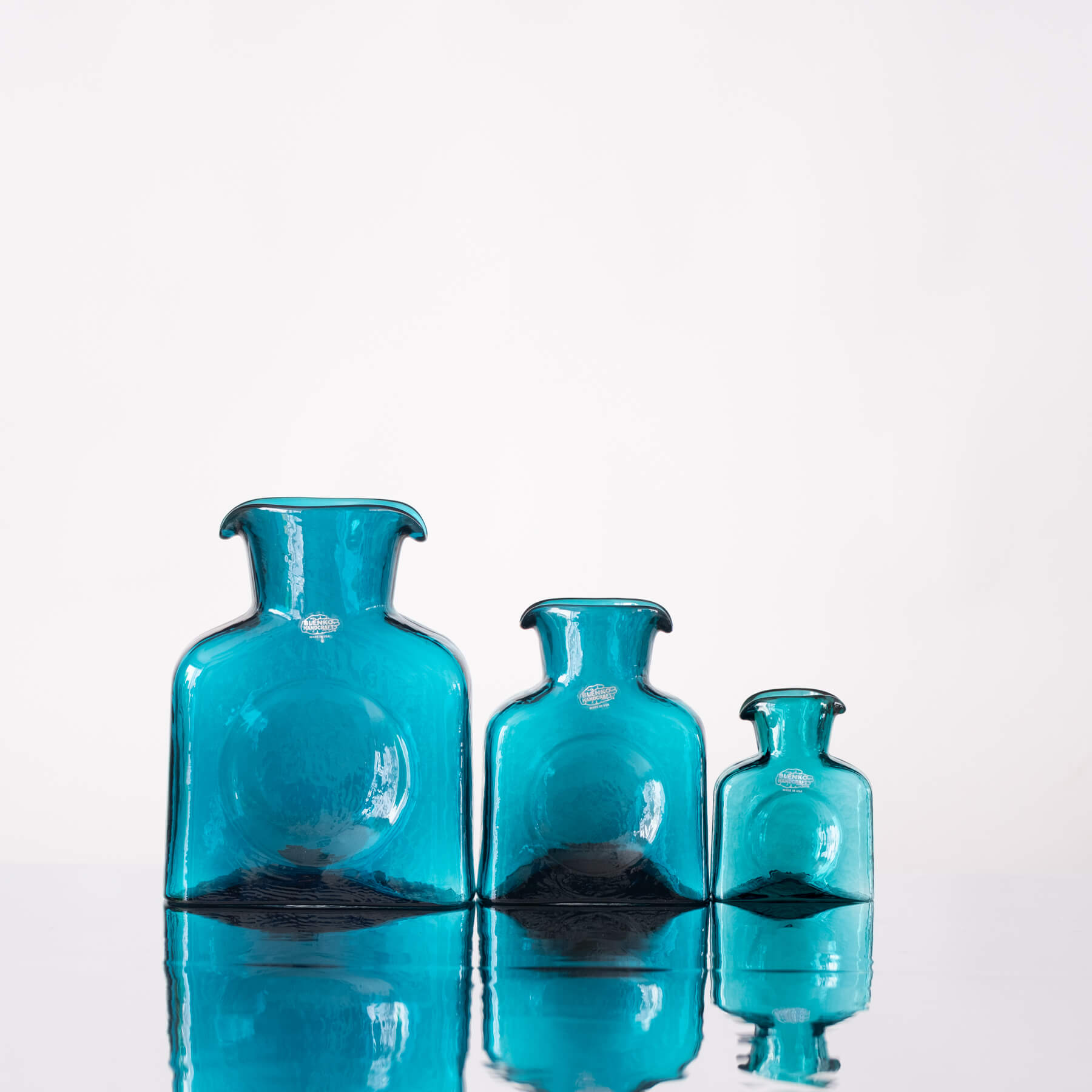 Three turquoise glass bottles of varying sizes on a white background
