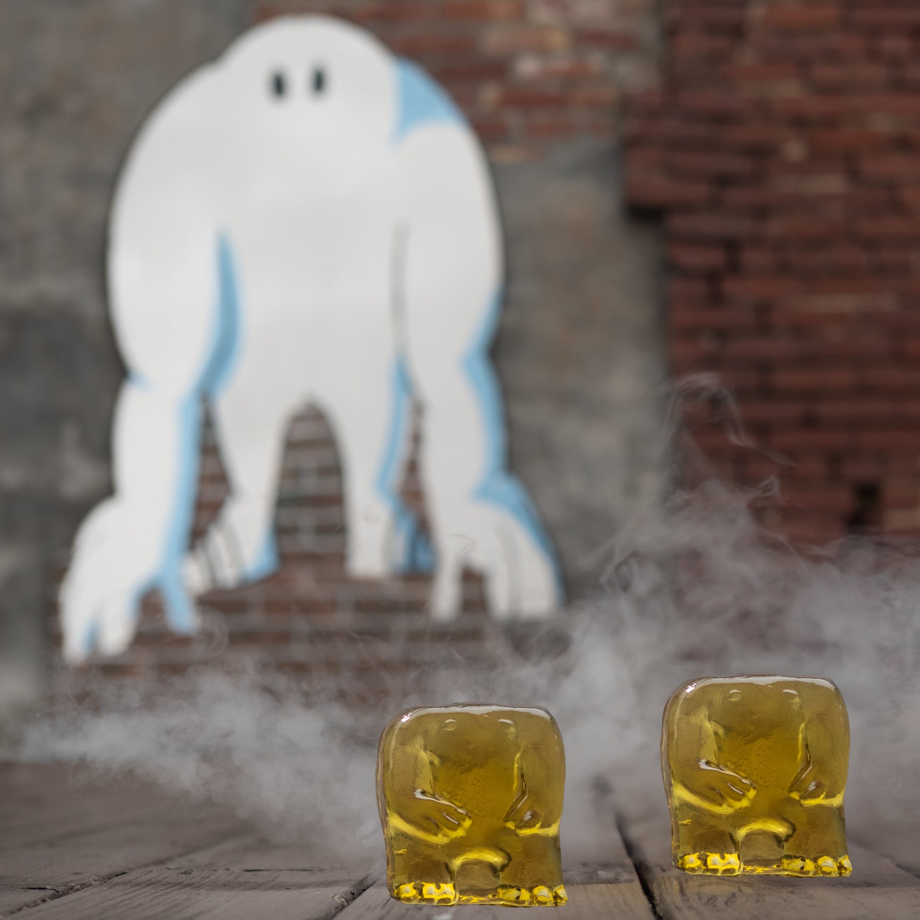 Two gold figurines on a wooden surface with a ghost and brick wall in the background.