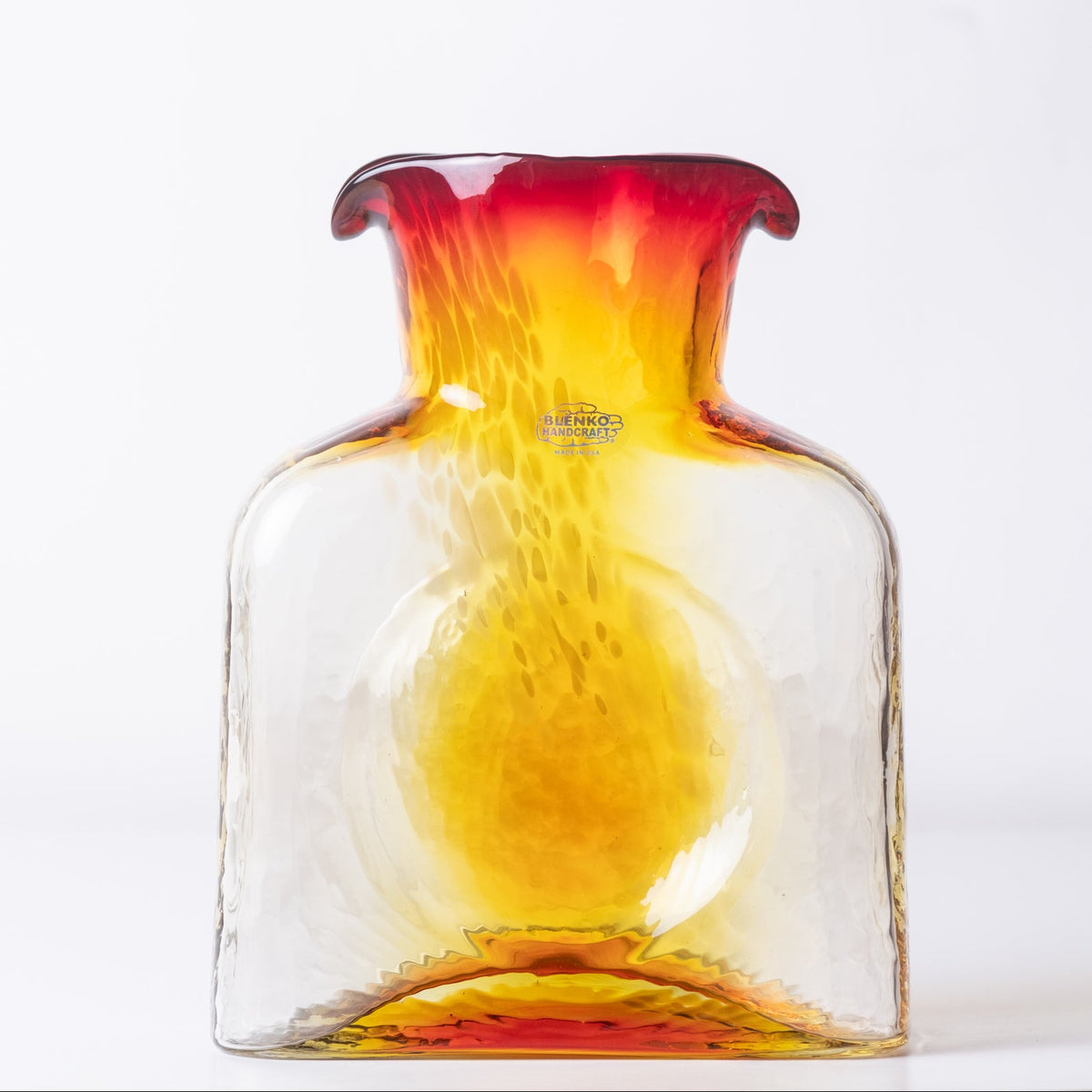 A hand-blown glass vase with a flared neck, featuring a gradient color transition from vibrant red at the top to bright yellow and clear glass at the bottom, set against a plain white background.