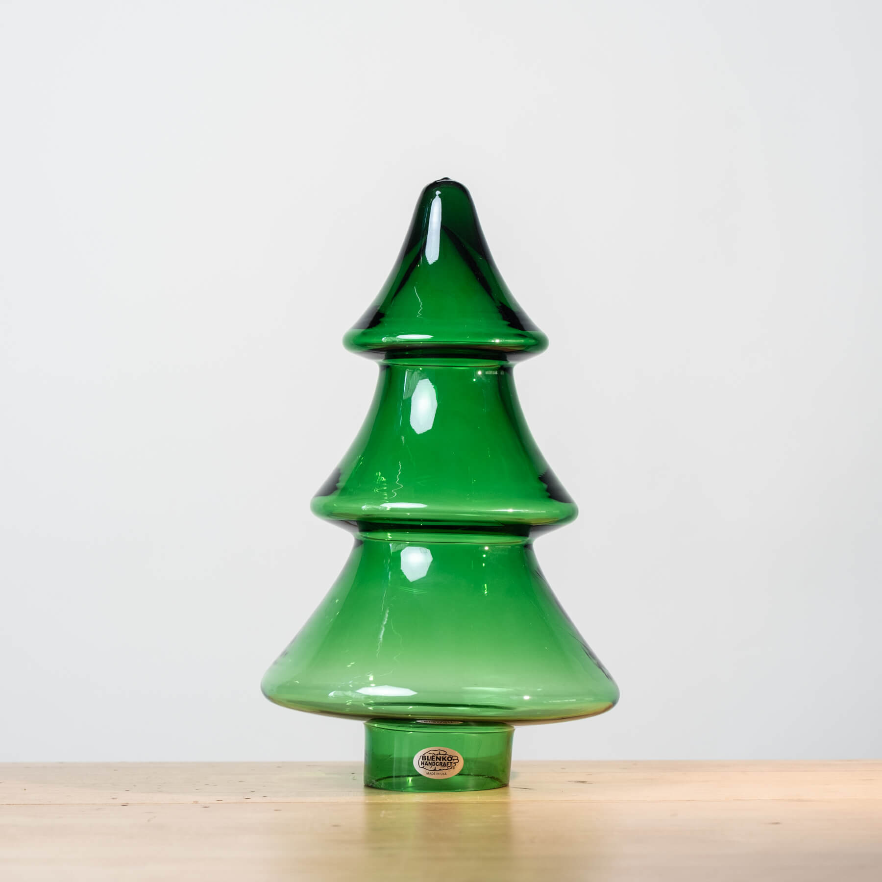 Green glass Christmas tree-shaped object on a light wooden surface with a white background
