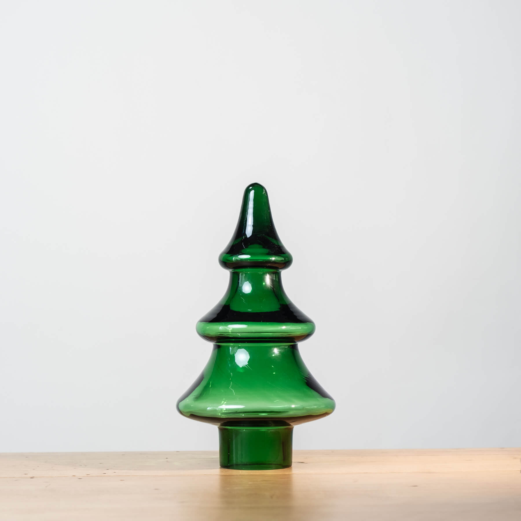 Green ceramic Christmas tree on a wooden surface with a light gray background