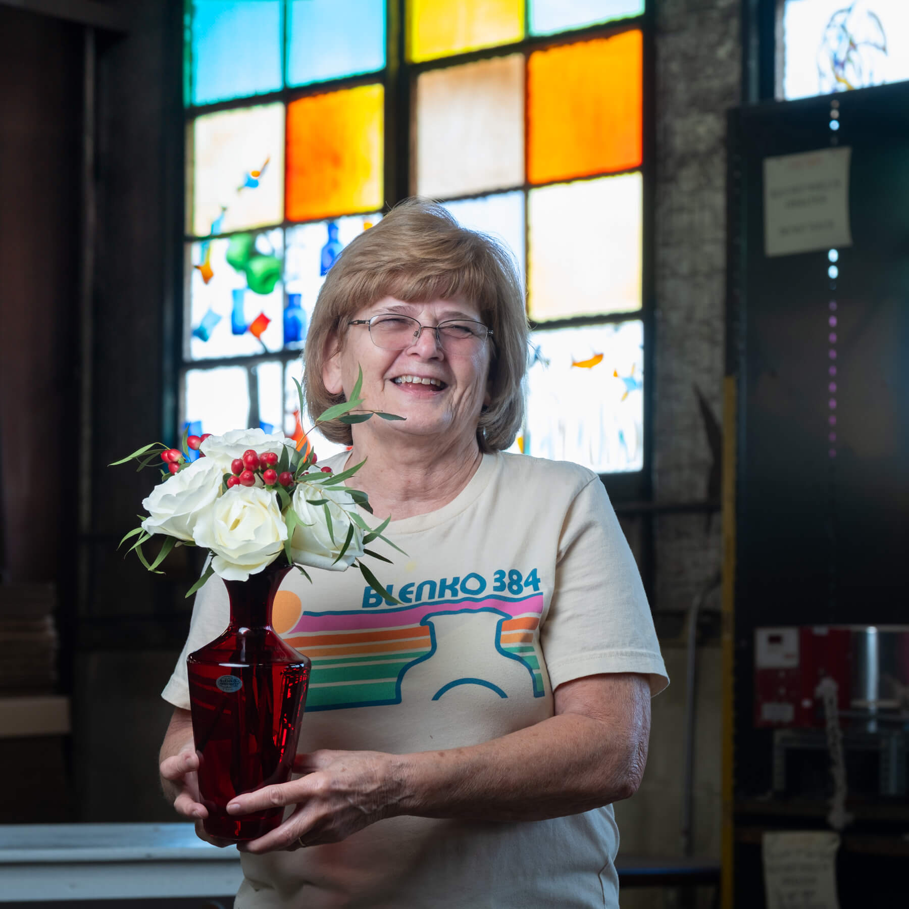 Woman holding a vase with flowers in front of a stained glass window