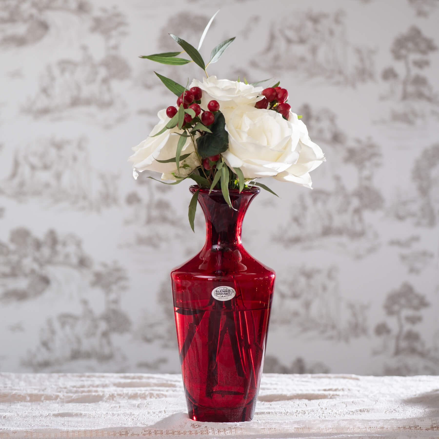 Red vase with white flowers and red berries on a textured surface