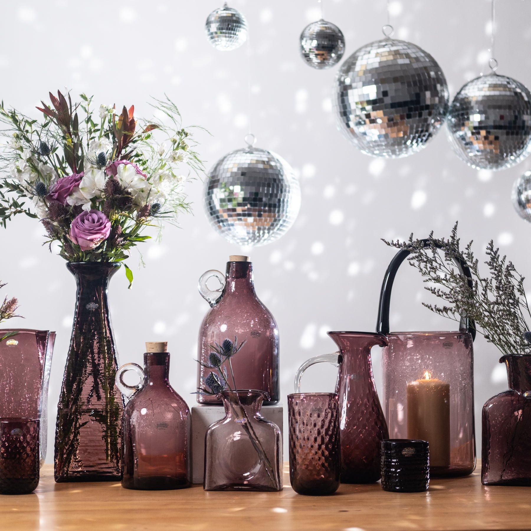 Decorative table setting with vases, bottles, and flowers against a disco ball and string light background.
