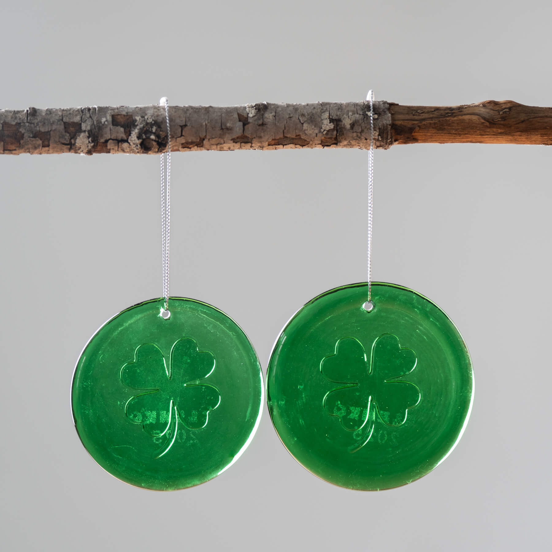Two green glass shamrock suncatchers hanging from strings, displayed against a neutral background.
