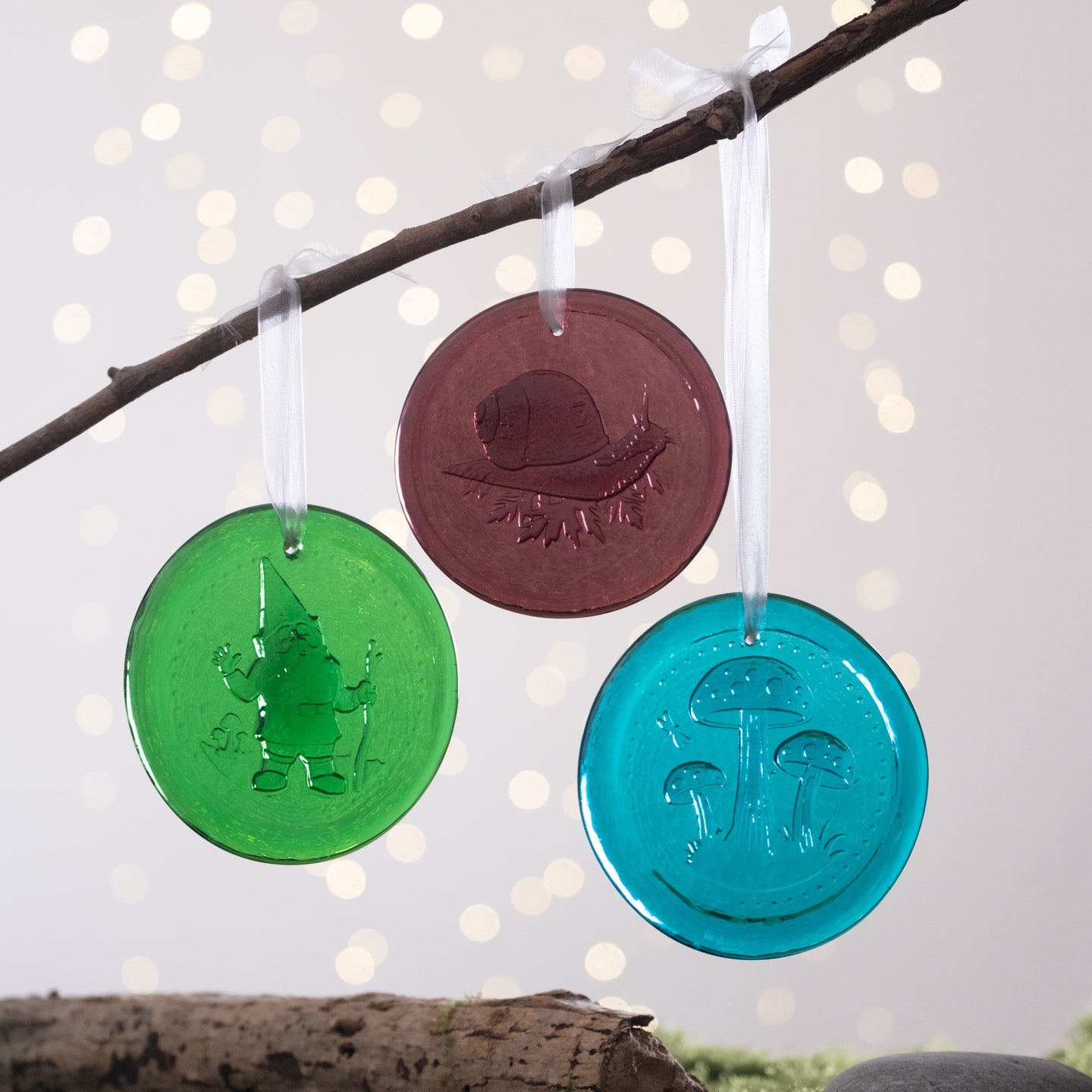 Three colorful round ornaments hanging on a branch with a blurred light background
