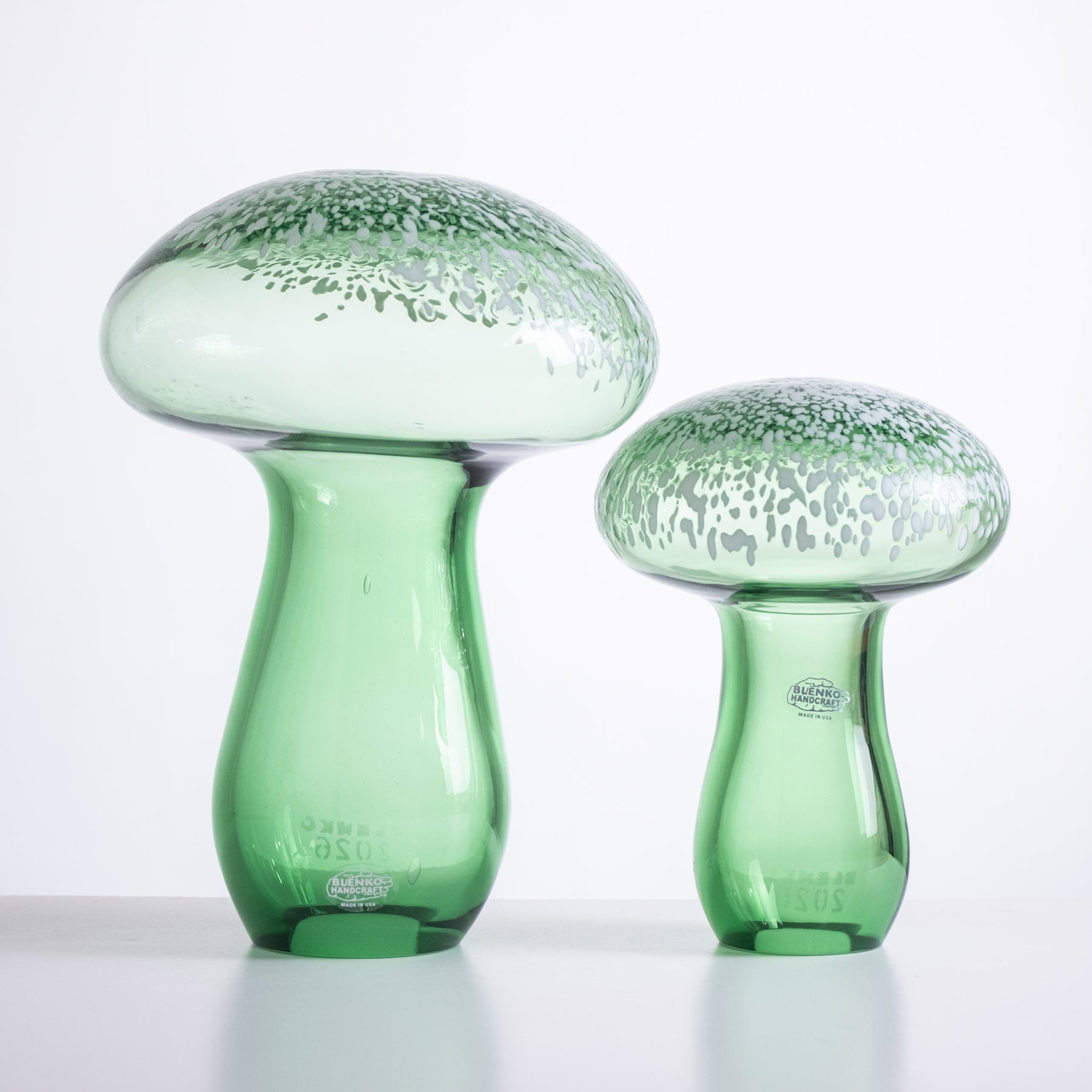 Two green glass mushroom-shaped objects on a white background