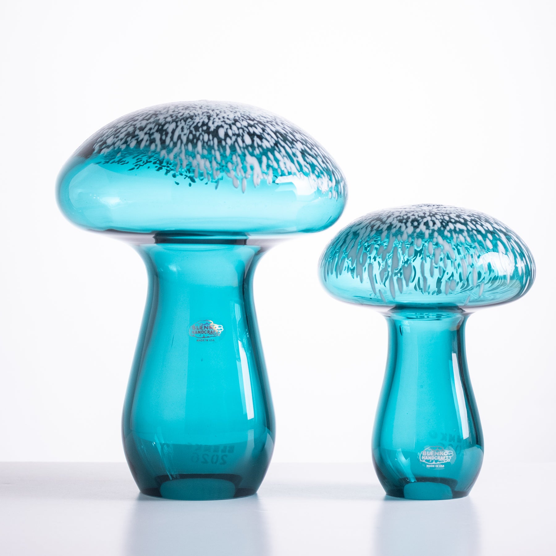 Two blue glass mushroom sculptures on a white background
