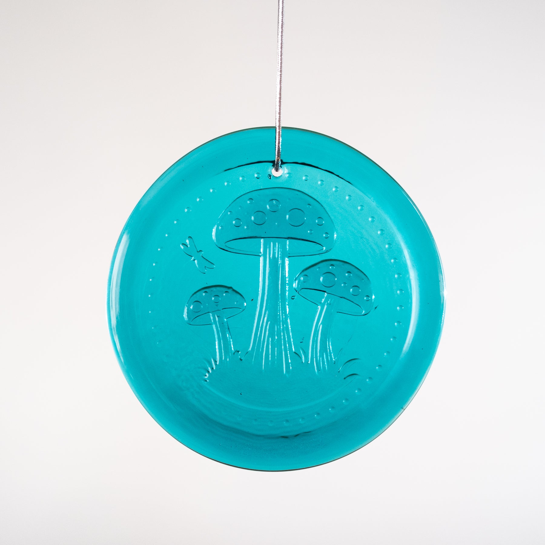 Turquoise circular ornament with mushroom design on a white background