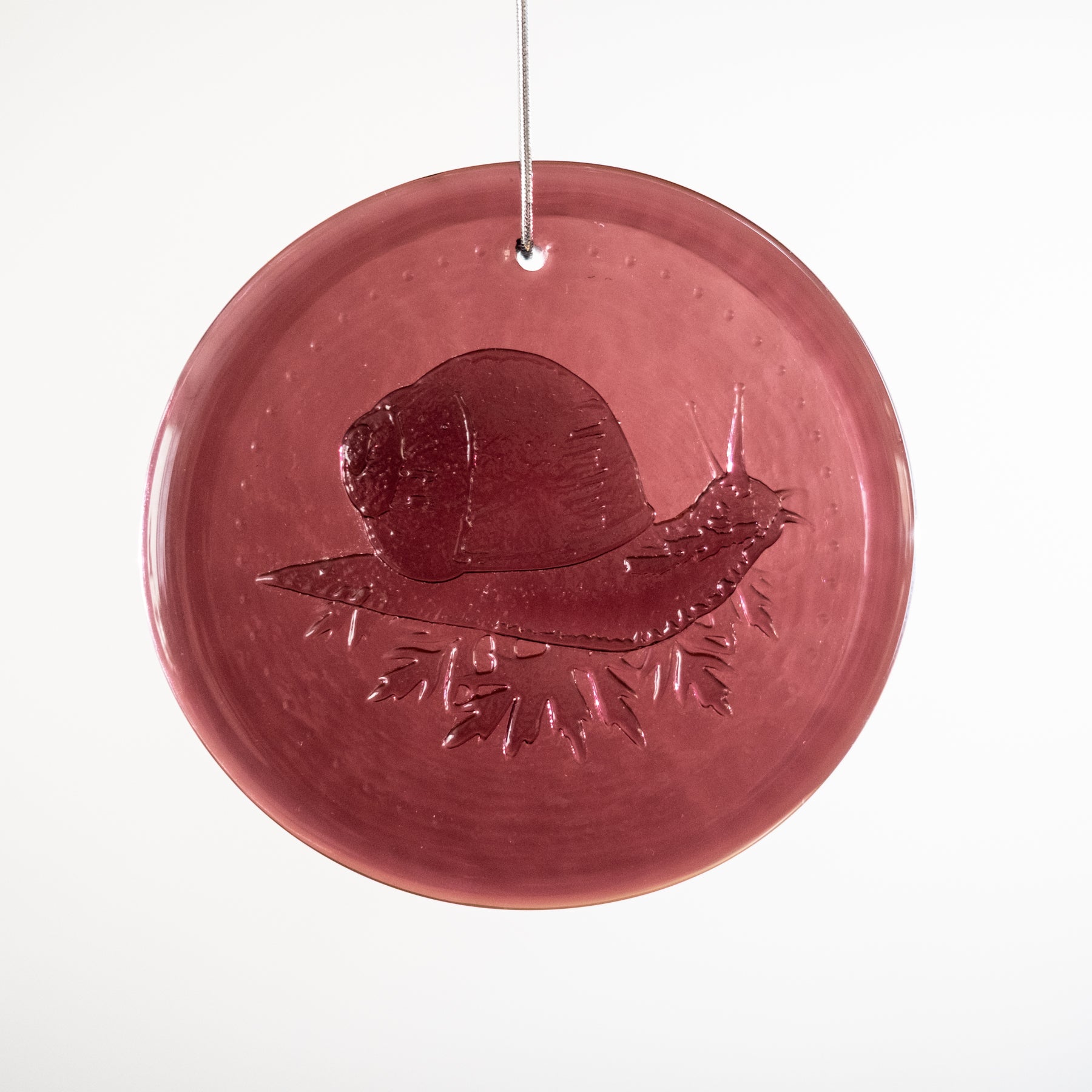 Round red glass ornament with a snail design on a white background