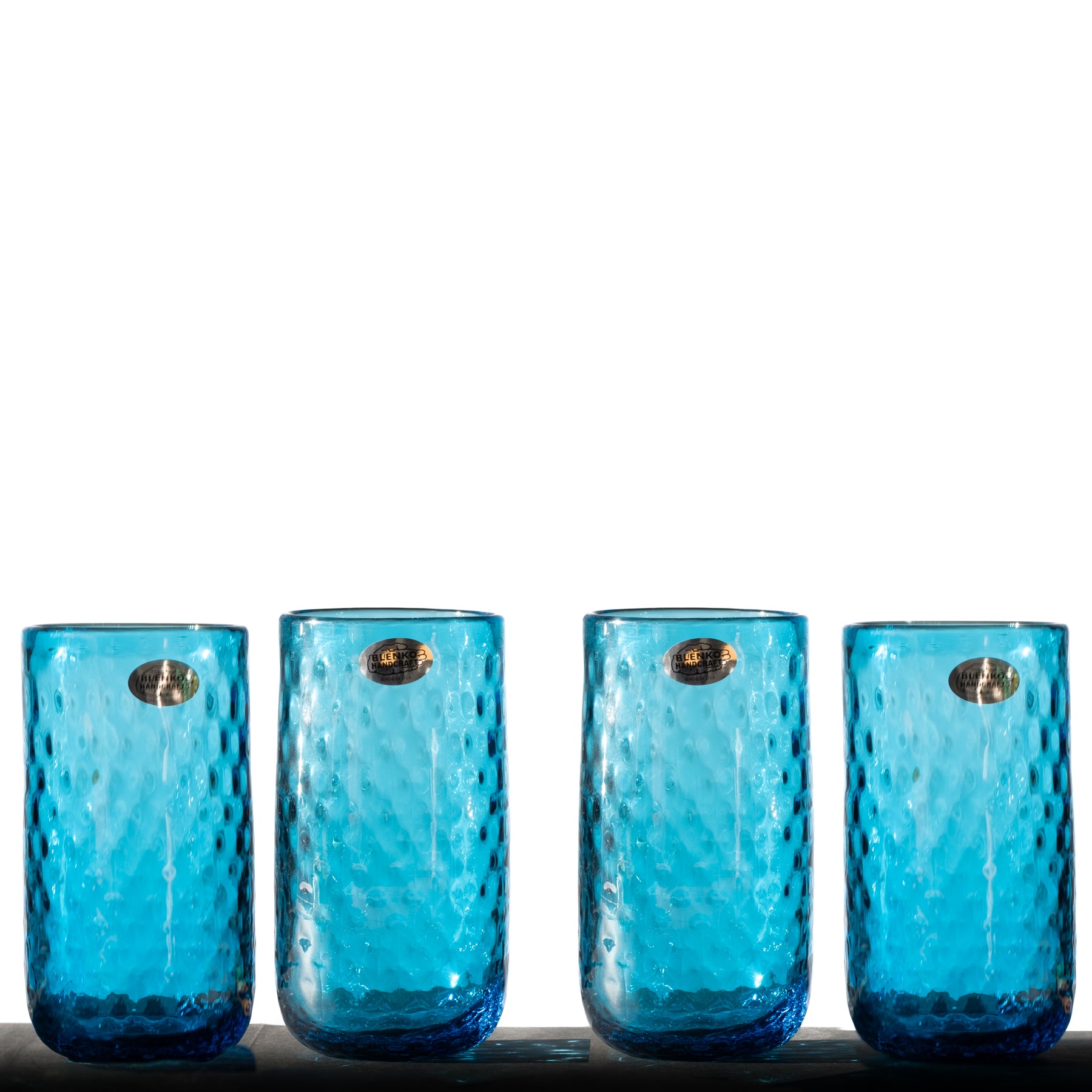A set of four turquoise colored glass tumblers with a diamond optic pattern displayed side by side.