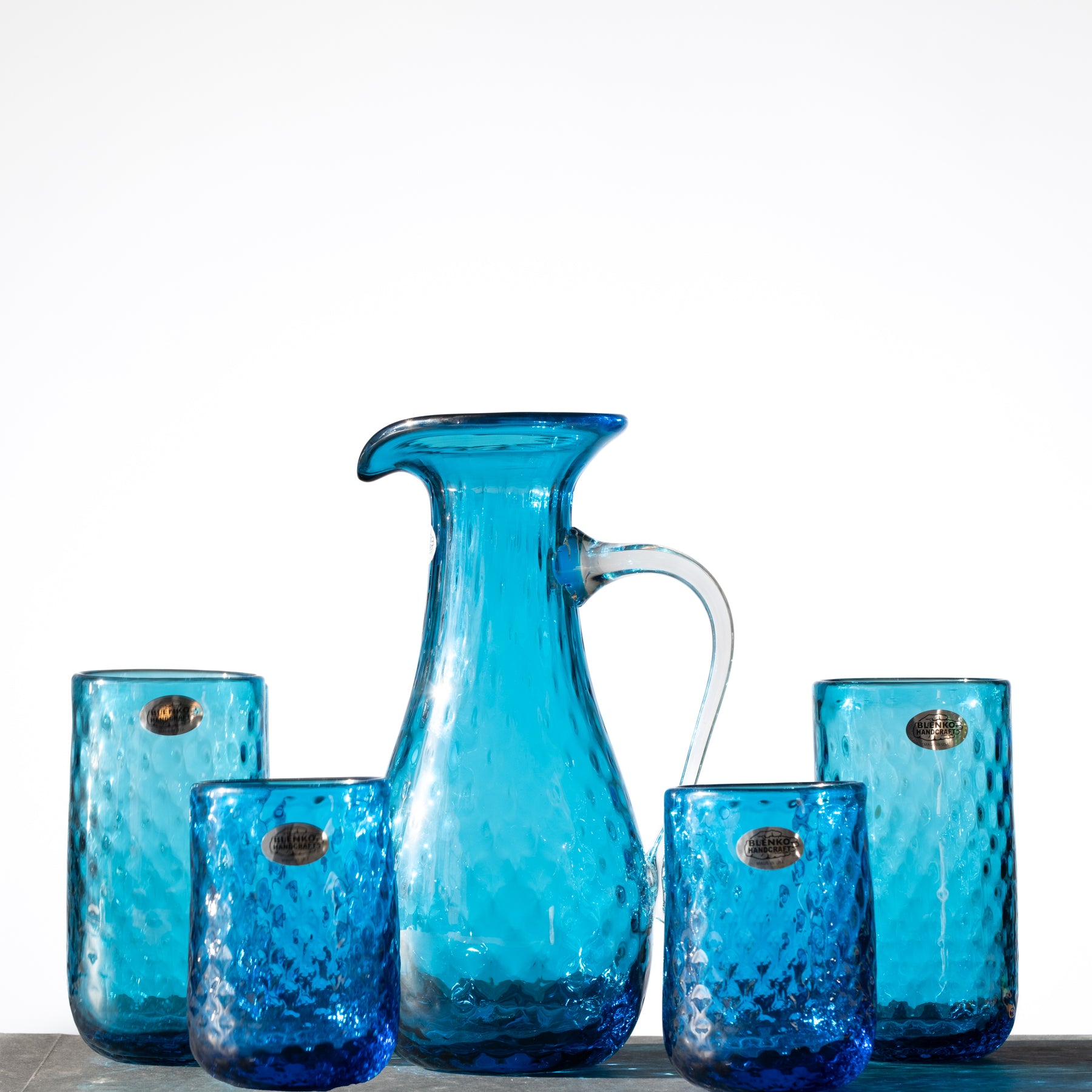 A set of turquoise glass drinkware, including a pitcher and multiple tumblers with a diamond optic texture pattern.