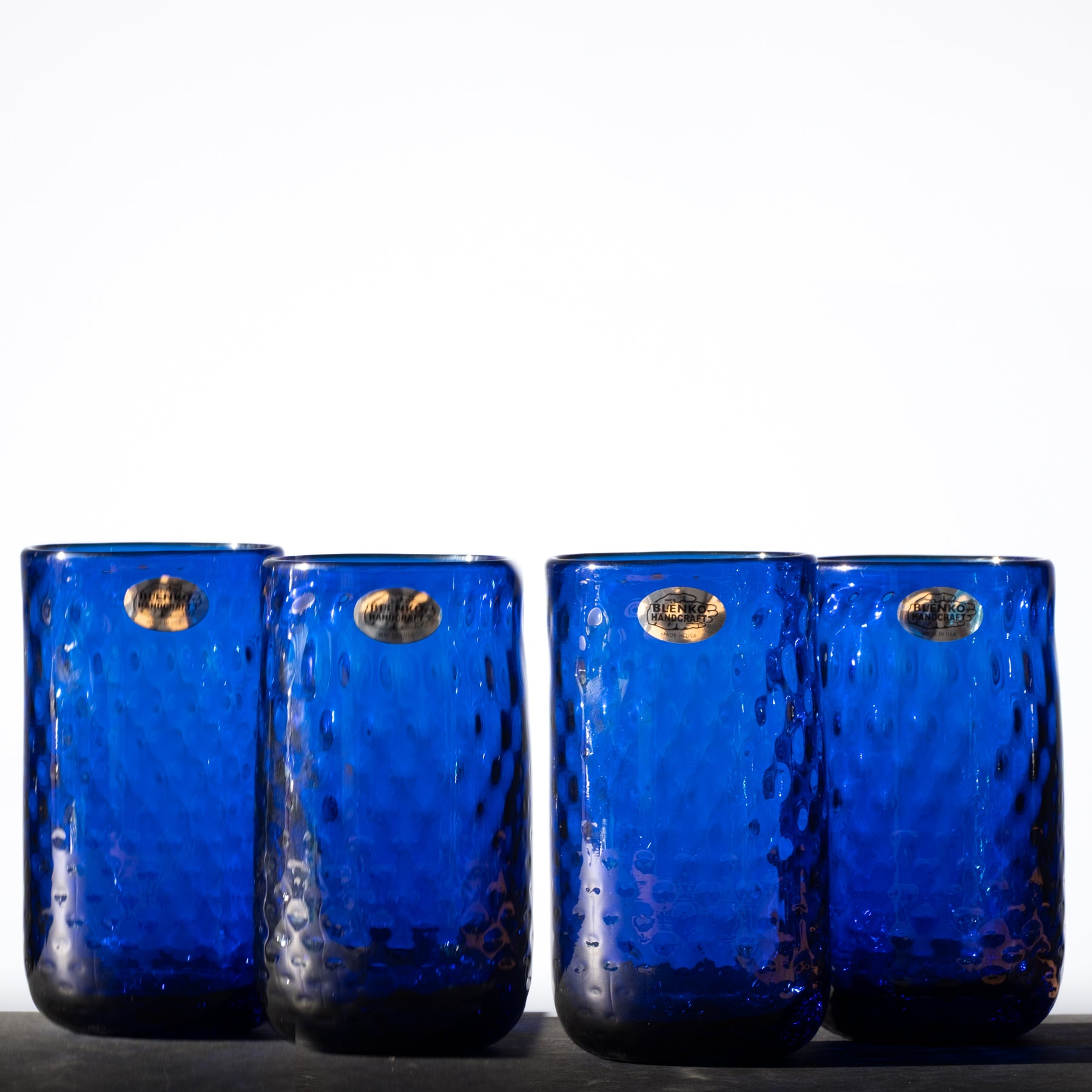 A set of four cobalt blue, hand-blown glass tumblers with a diamond optic pattern.
