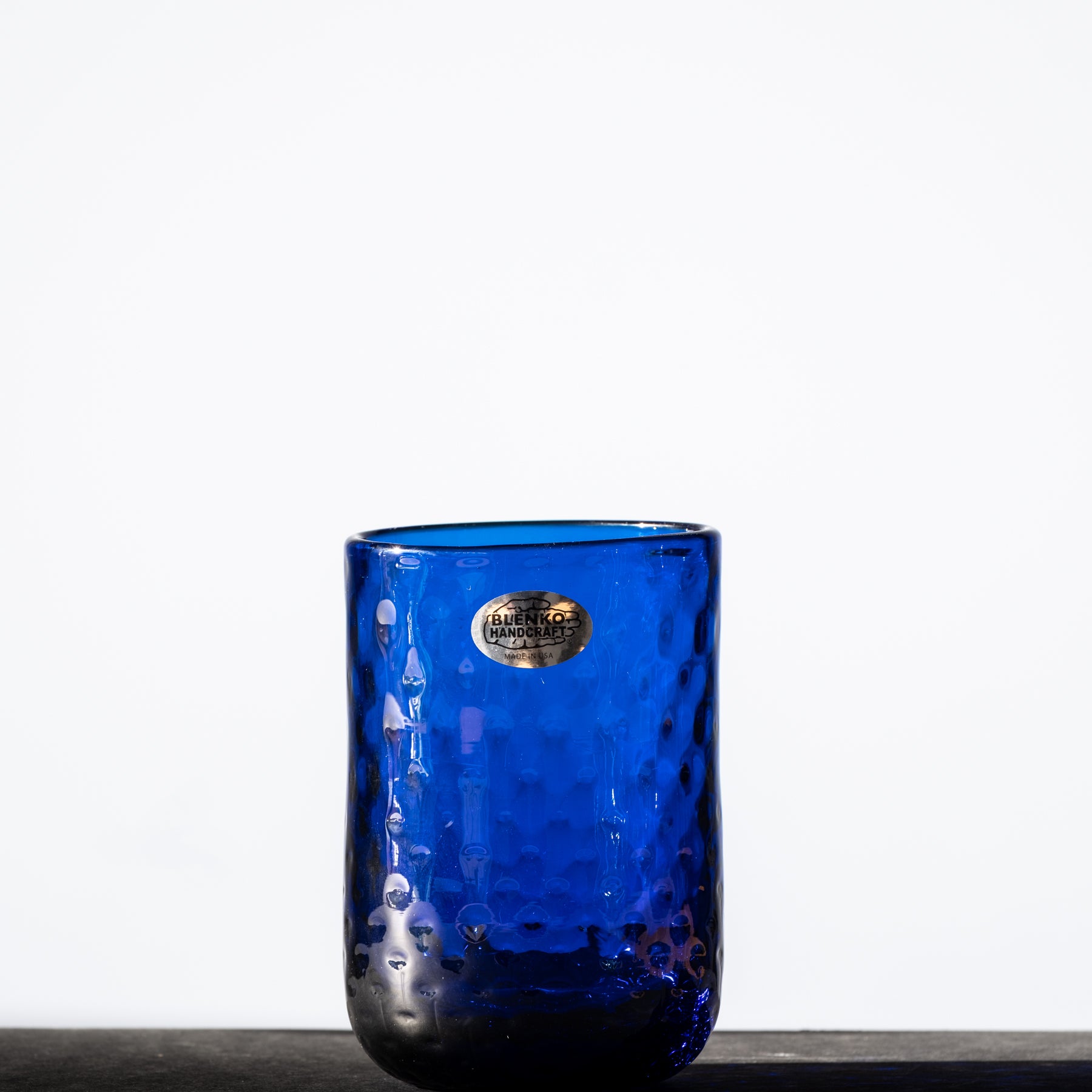 A blue glass tumbler with a diamond optic pattern, displaying a reflection on its surface.