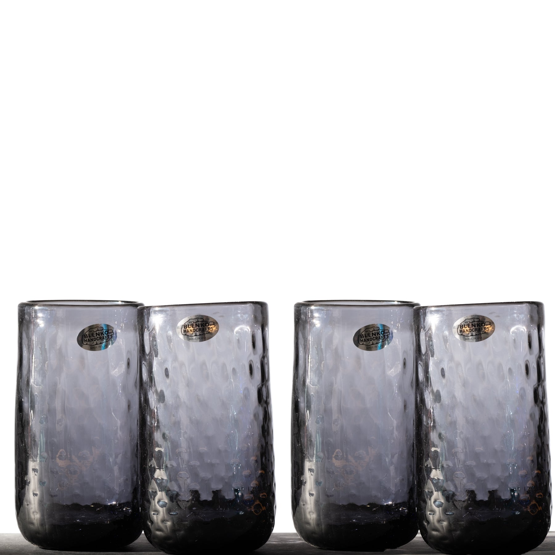 A set of four clear glass tumblers with a diamond optic pattern, displayed side by side.