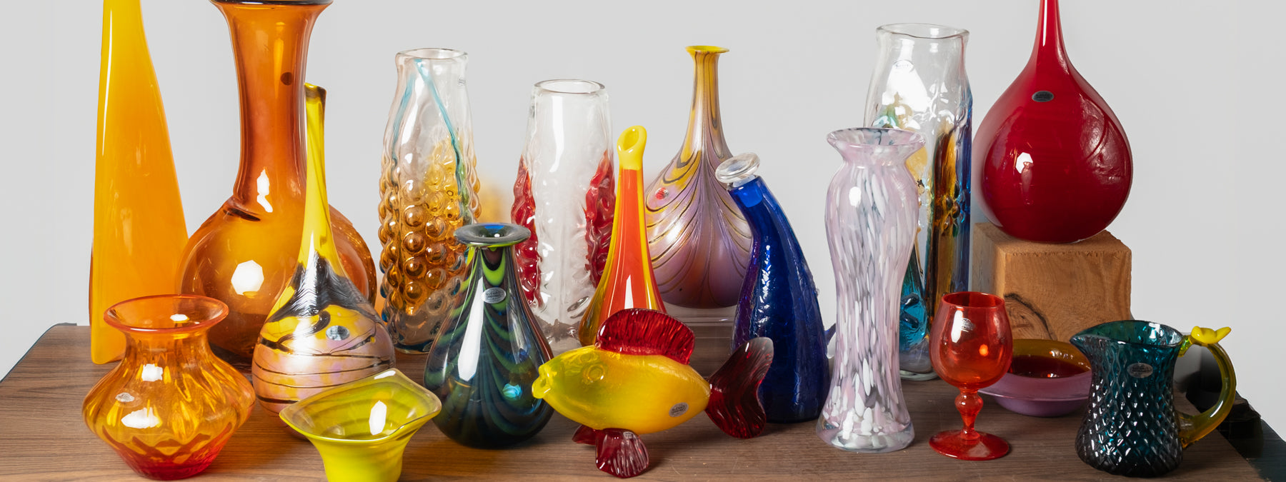 Collection of colorful glass vases on a wooden surface with a white background