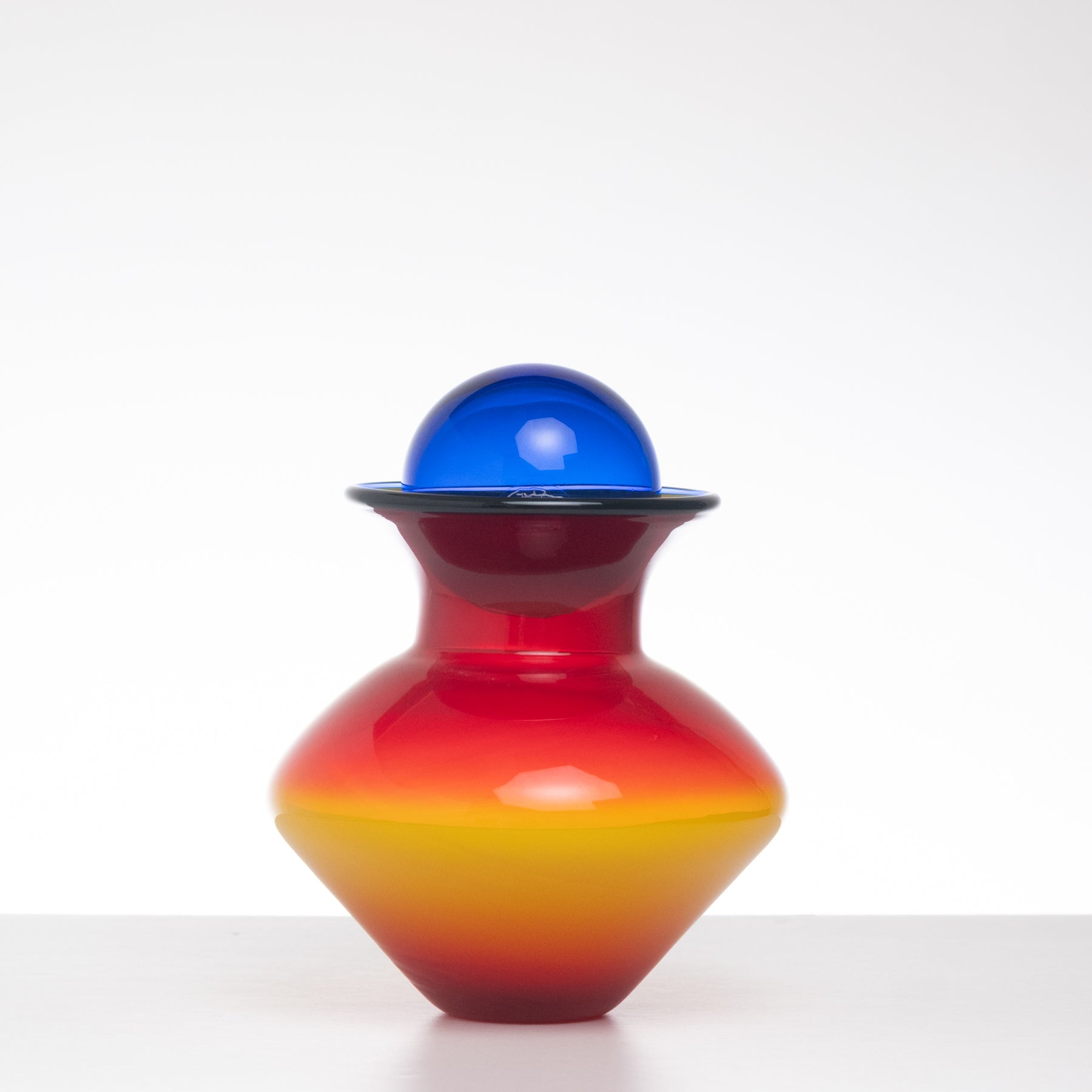 Colorful glass vase with red, yellow, and blue gradient on a white background