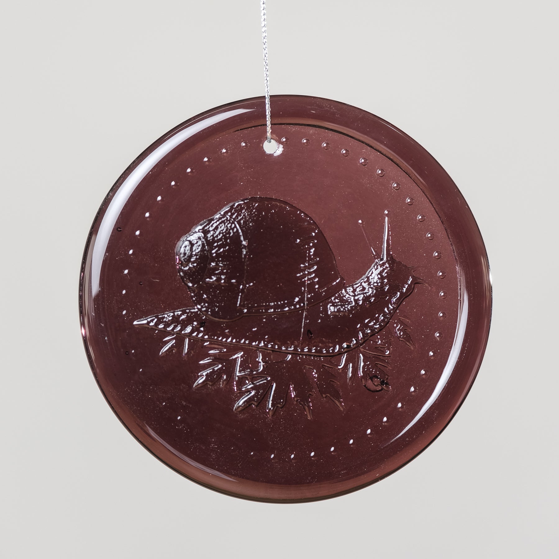 Round brown decorative item with a design of a hat and leaves on a light gray background