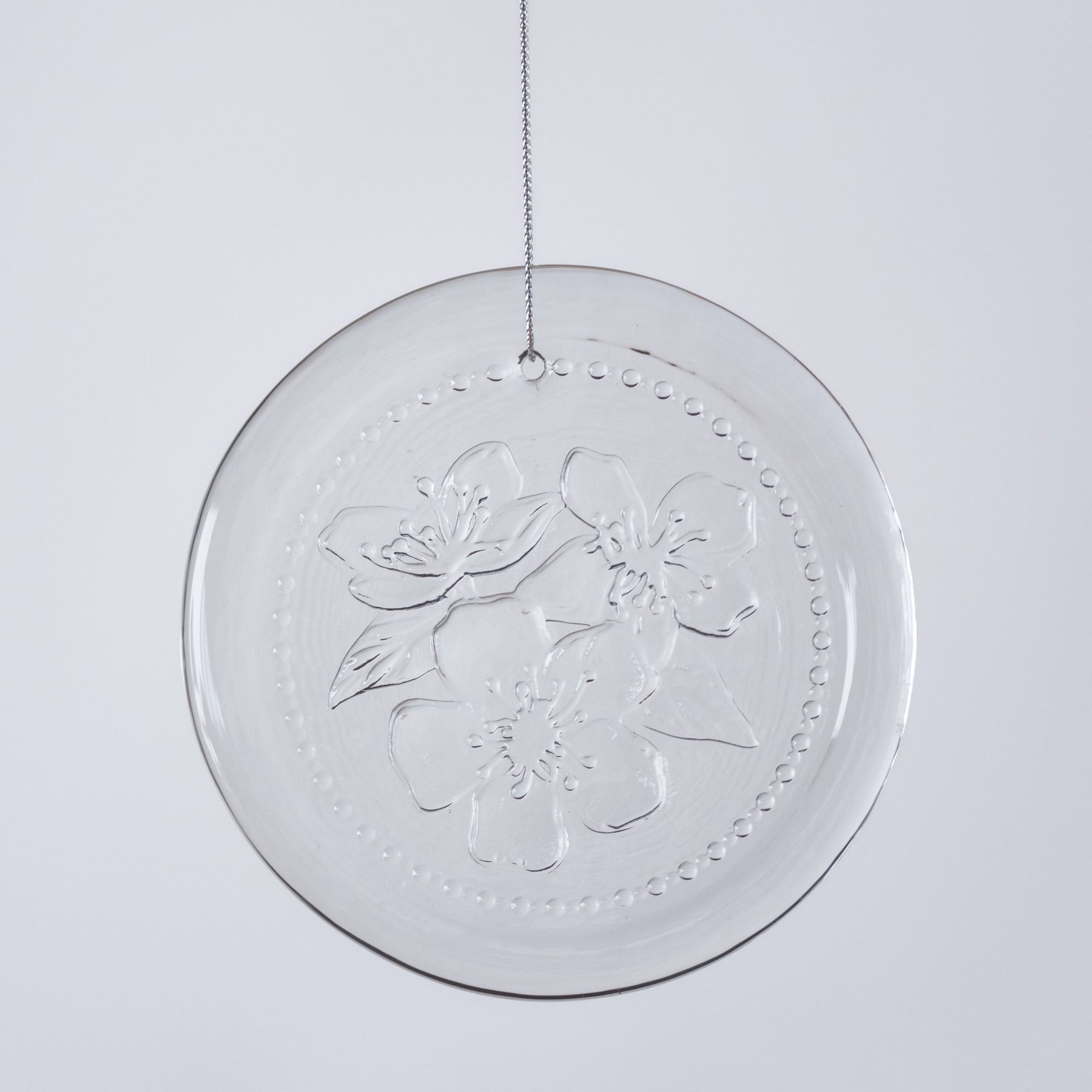 Clear circular decorative item with floral embossing on a light gray background