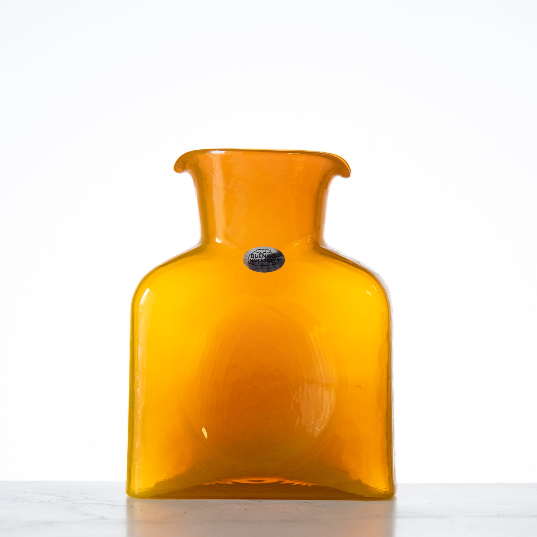 A tall, amber-colored glass water bottle with a narrow neck, displayed against a light background.