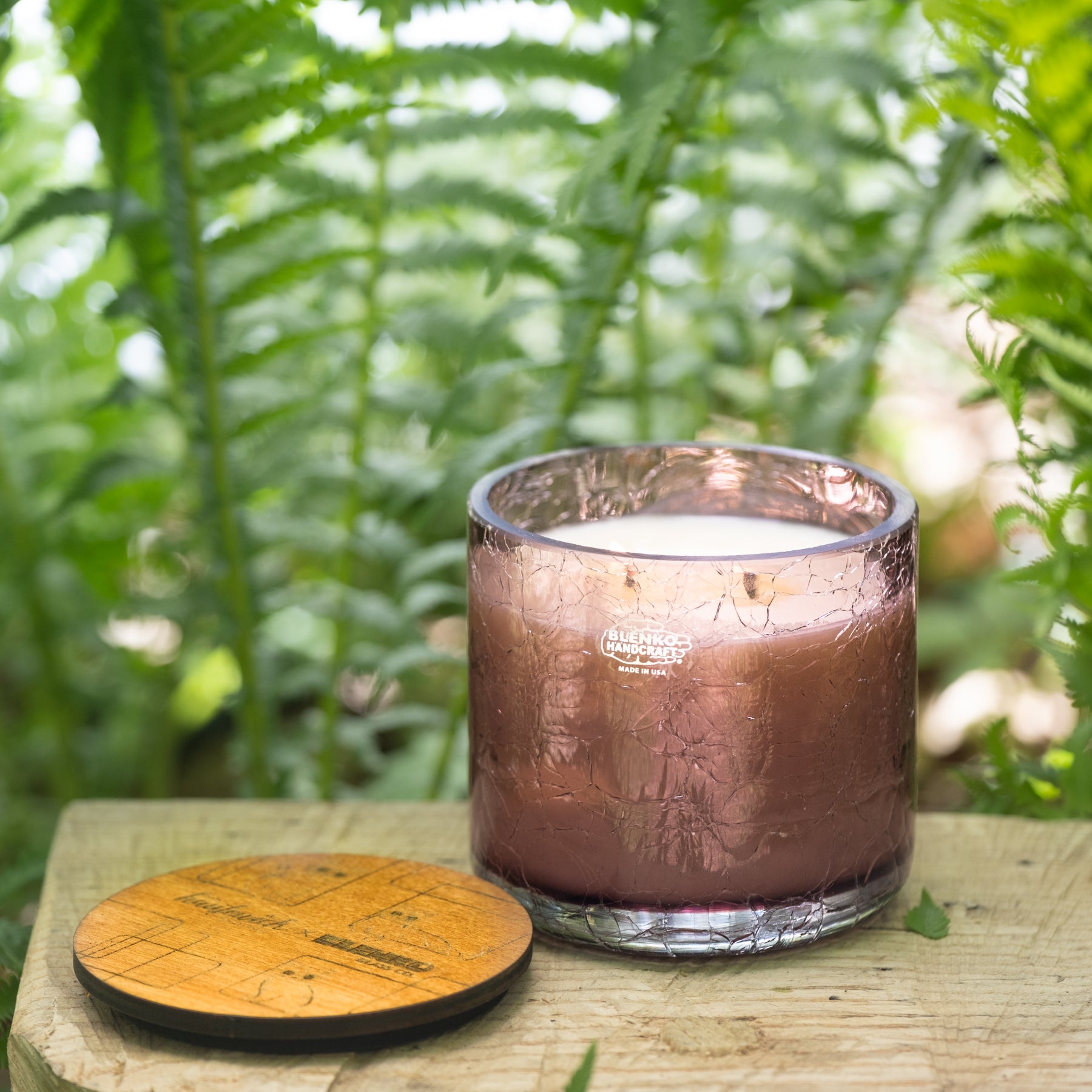 Candle in a textured glass jar on a wooden surface with a natural background