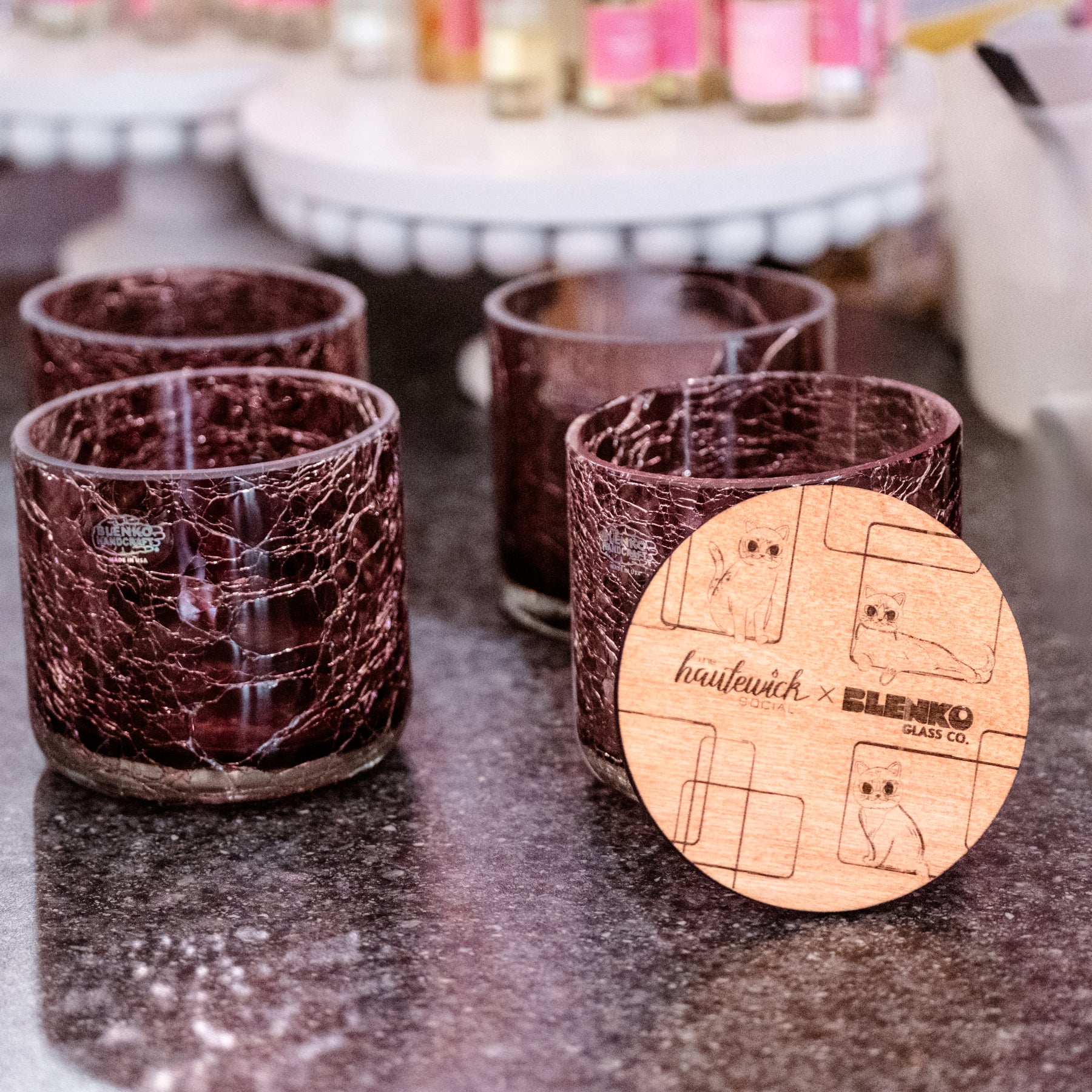 Set of glass tumblers with a wooden coaster featuring brand logos on a dark surface.