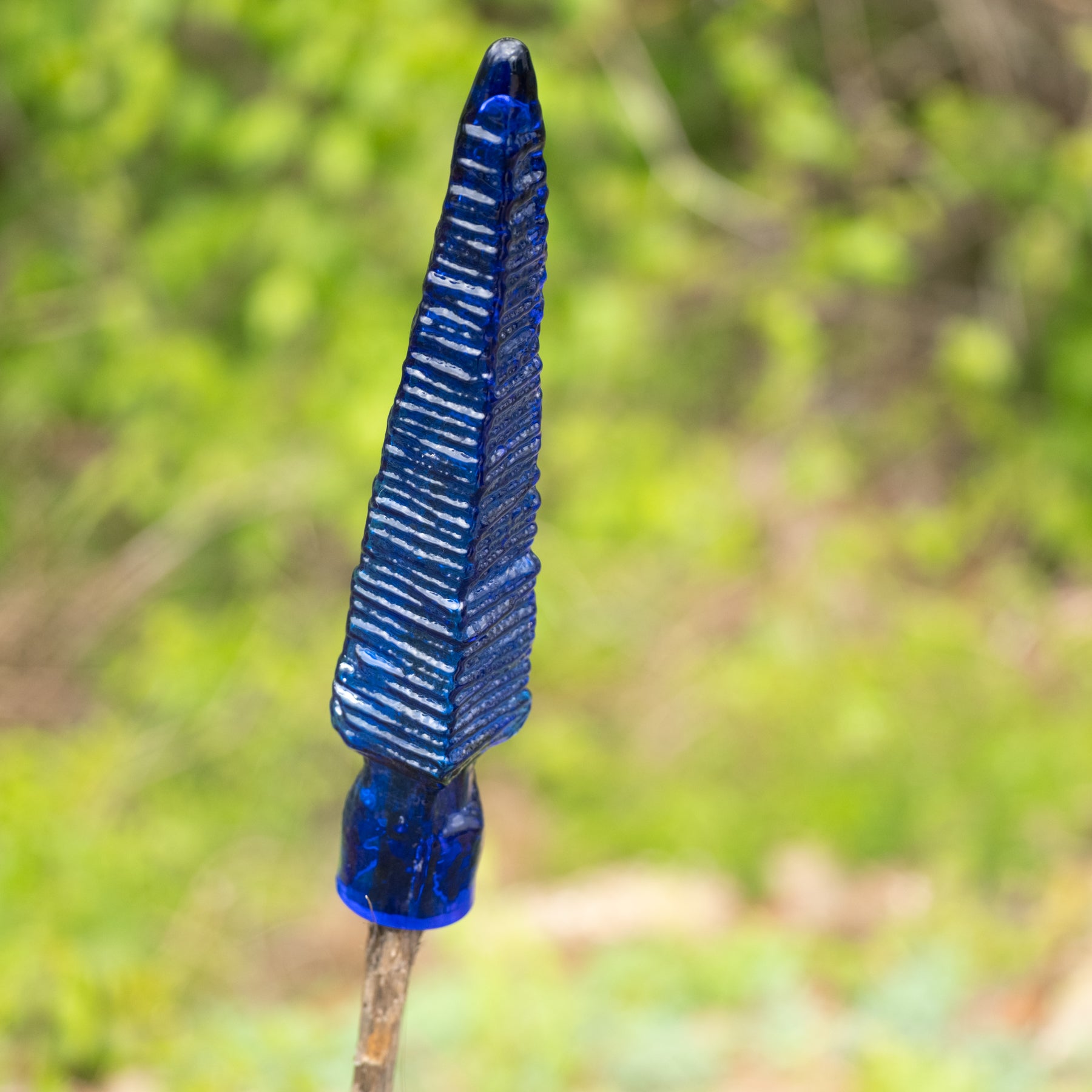 Blue glass arrowhead against a blurred green natural background