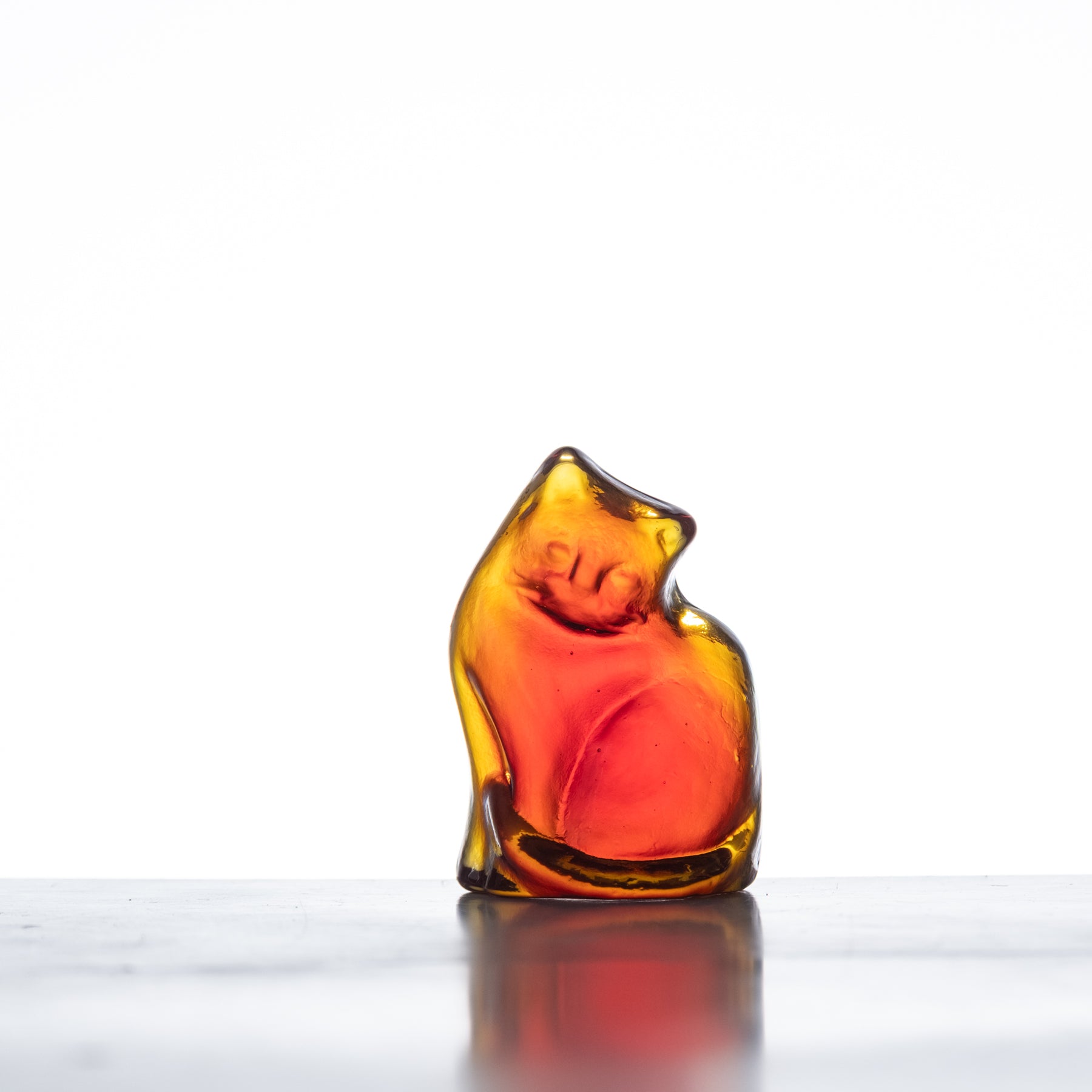 A handcrafted glass figurine of a cat with a tangerine orange color, showing a whimsical and playful design.