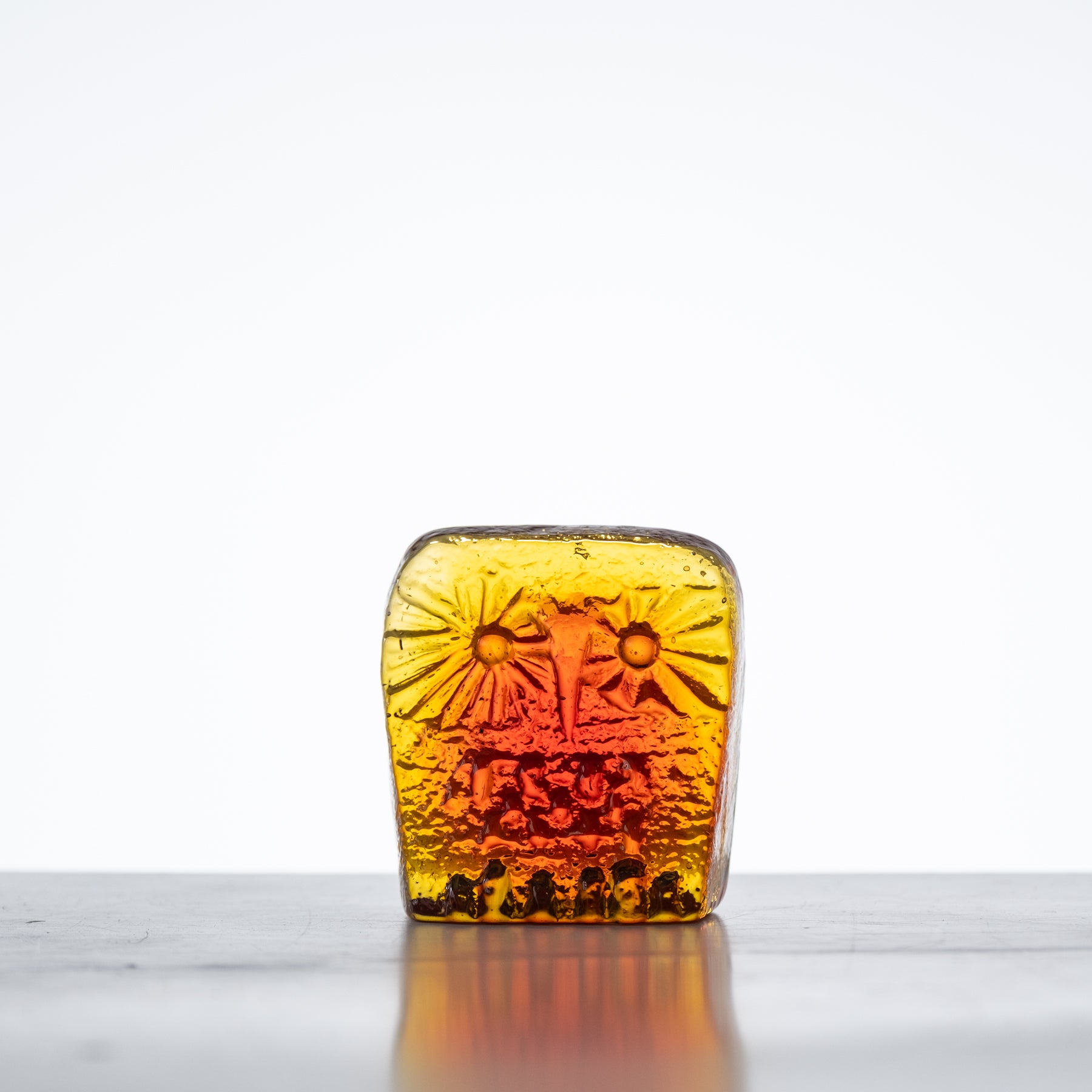 A small tangerine-colored glass owl figurine with a flat back, placed on a reflective surface.