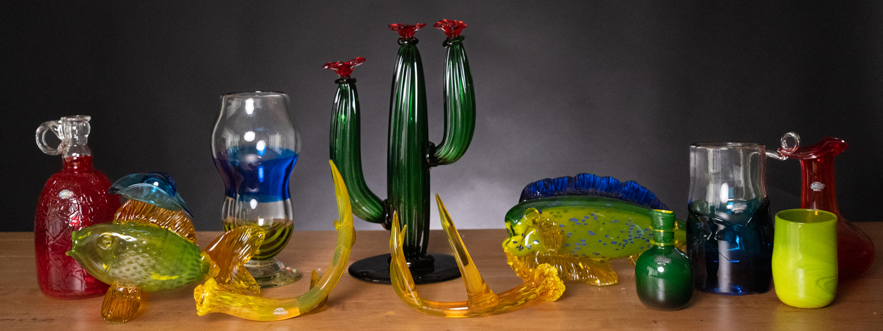 Collection of colorful glass art pieces on a wooden surface with a dark background