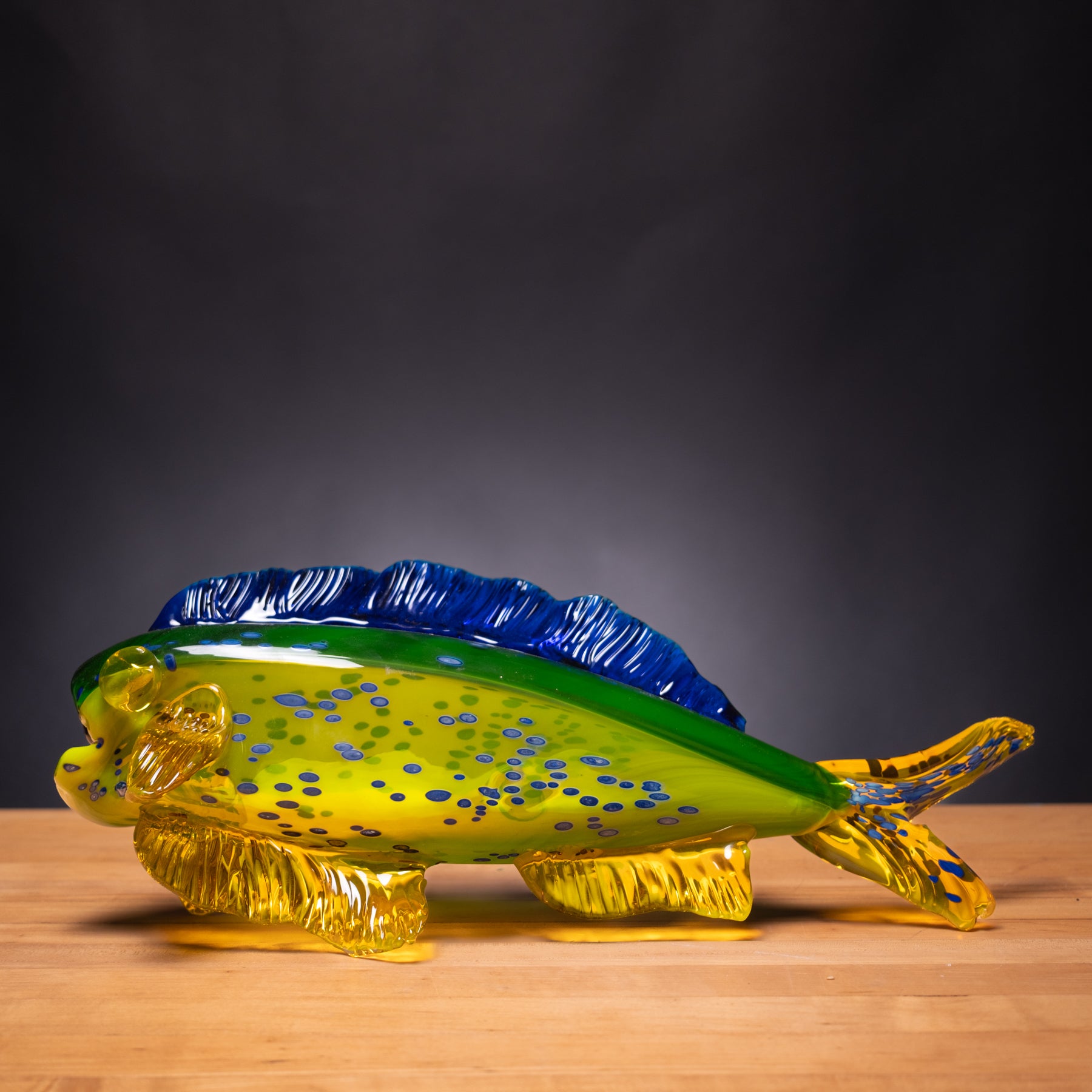 Glass sculpture of a fish with blue and green accents on a wooden surface