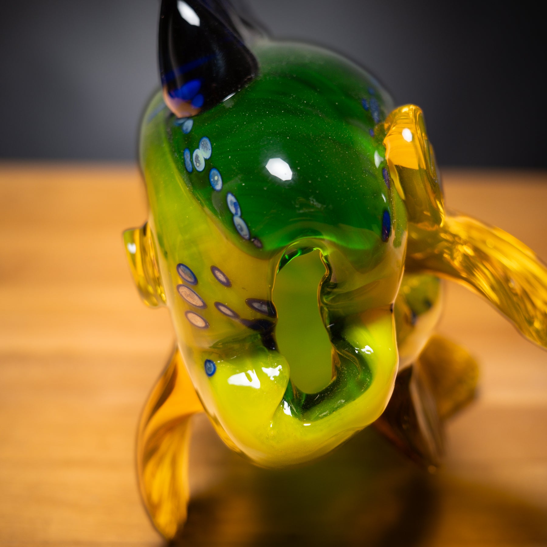 Glass sculpture of a fish with green body and yellow tail on a wooden surface