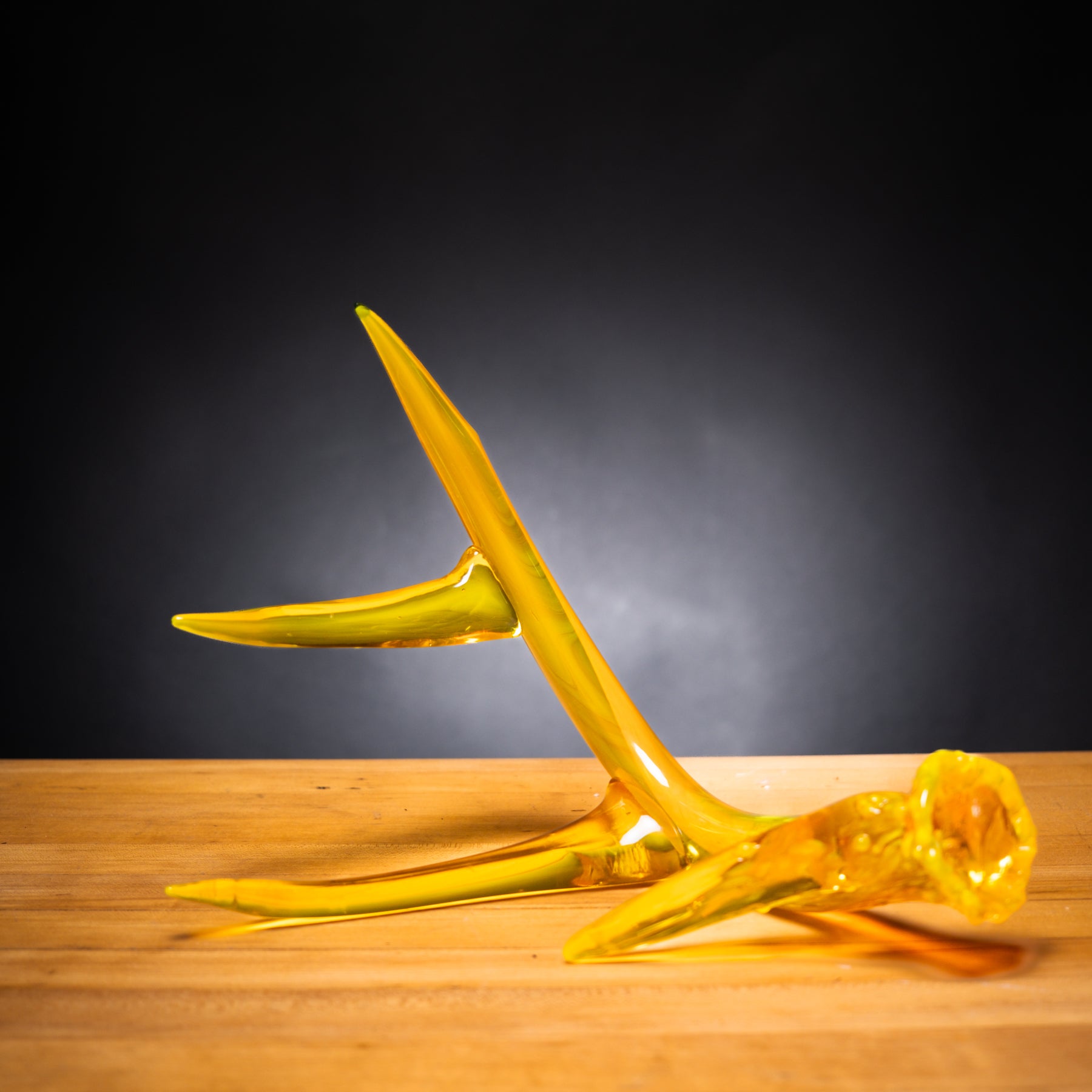 Yellow glass sculpture on a wooden surface with a dark background