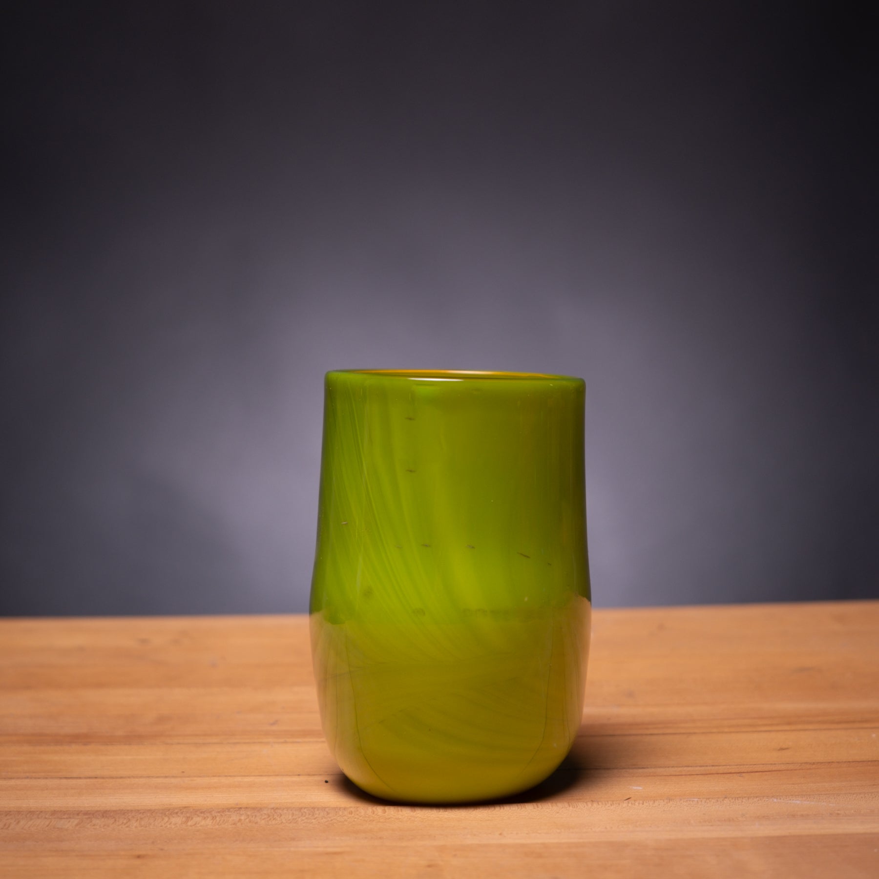 Green glass vase on a wooden surface with a dark gray background