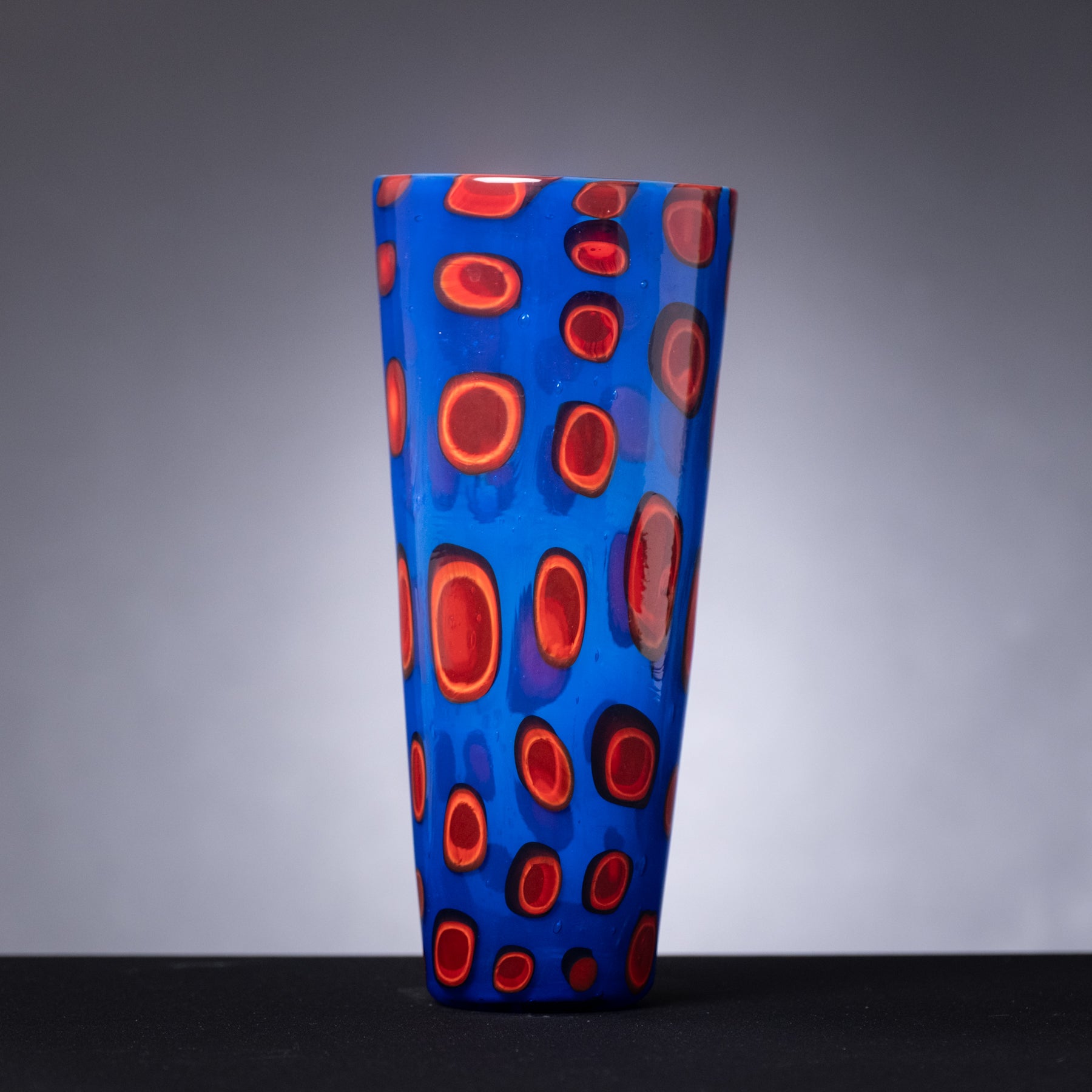 Blue glass vase with red circular patterns on a gray background