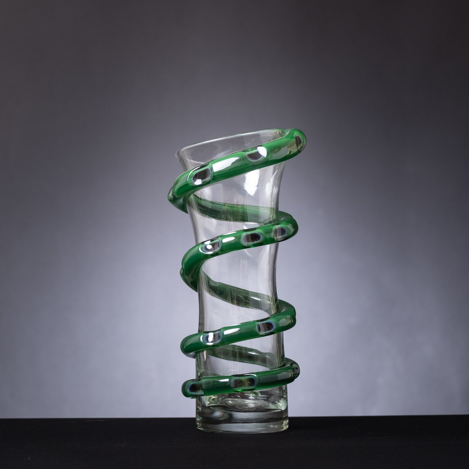 Glass vase with green spiral design on a gray background
