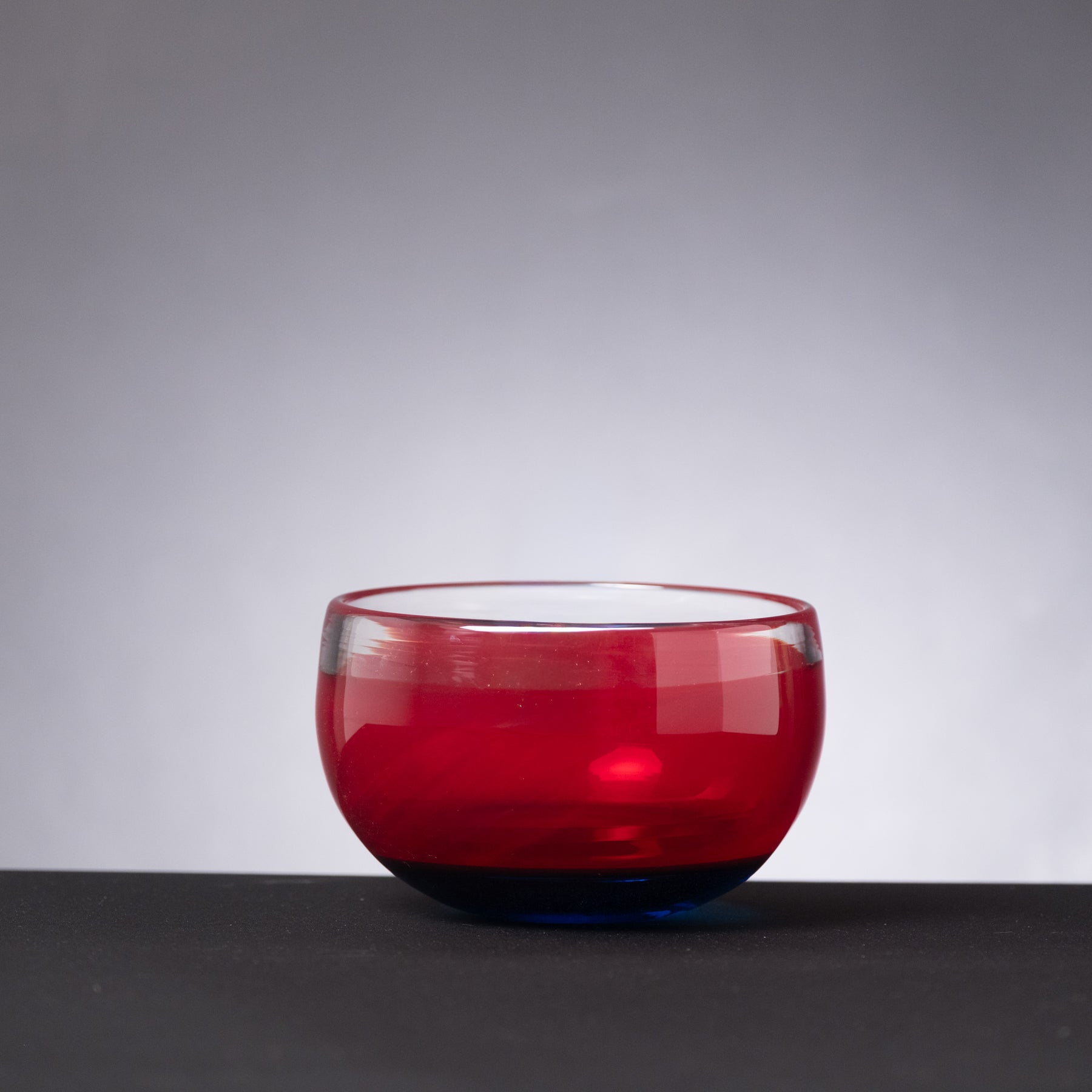 Red glass bowl on a dark surface with a gray background