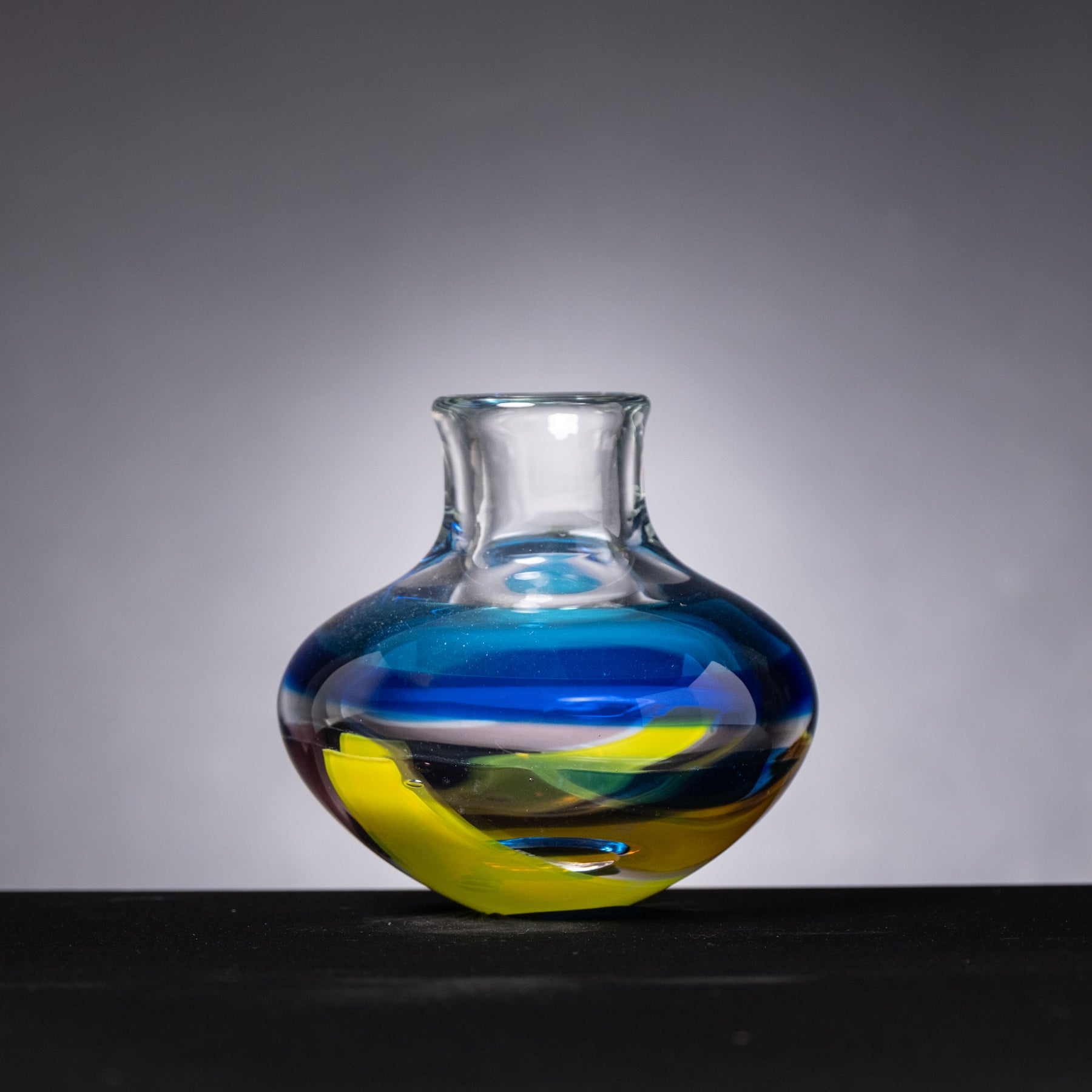 Glass vase with blue and yellow swirls on a gray background