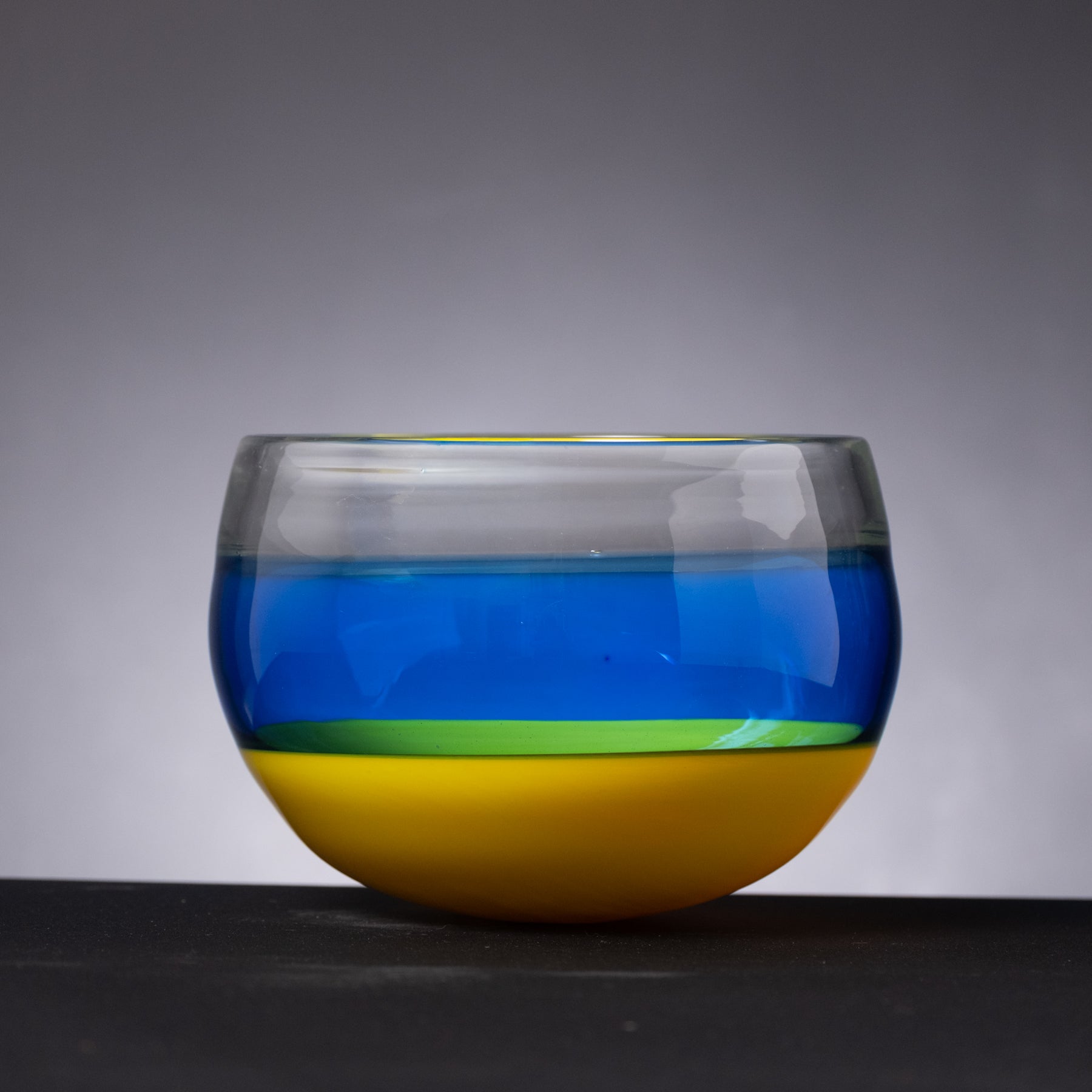Colorful glass bowl with blue, green, and yellow layers on a gray background