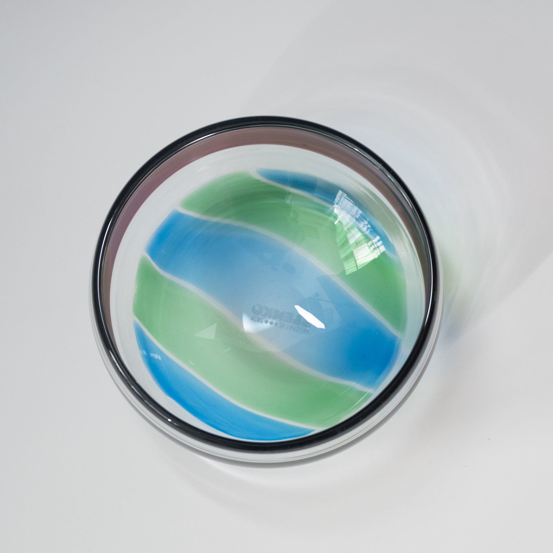 Round glass bowl with blue and green stripes on a white background