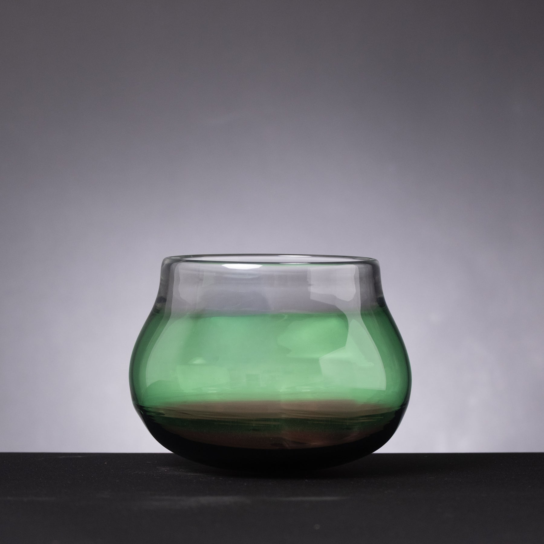 Green glass bowl on a dark surface with a gray background